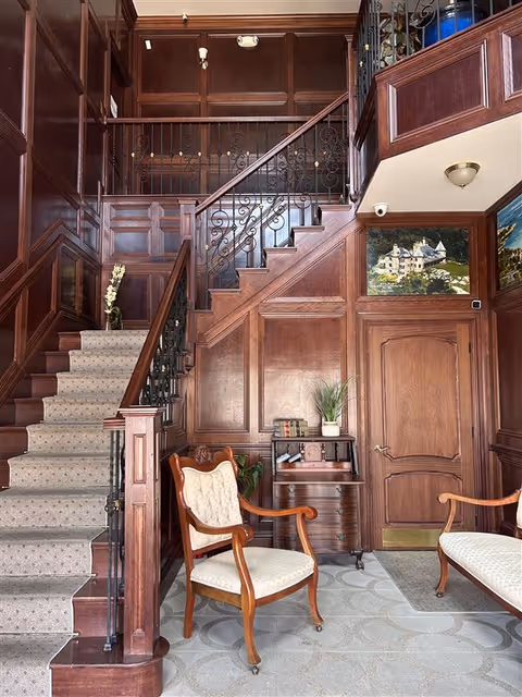 A grand wood-paneled foyer with staircase, ornate railing, and seating area.