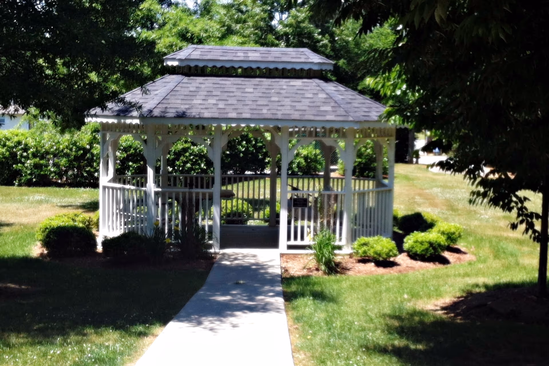 White gazebo in a manicured garden with a walkway to its entrance