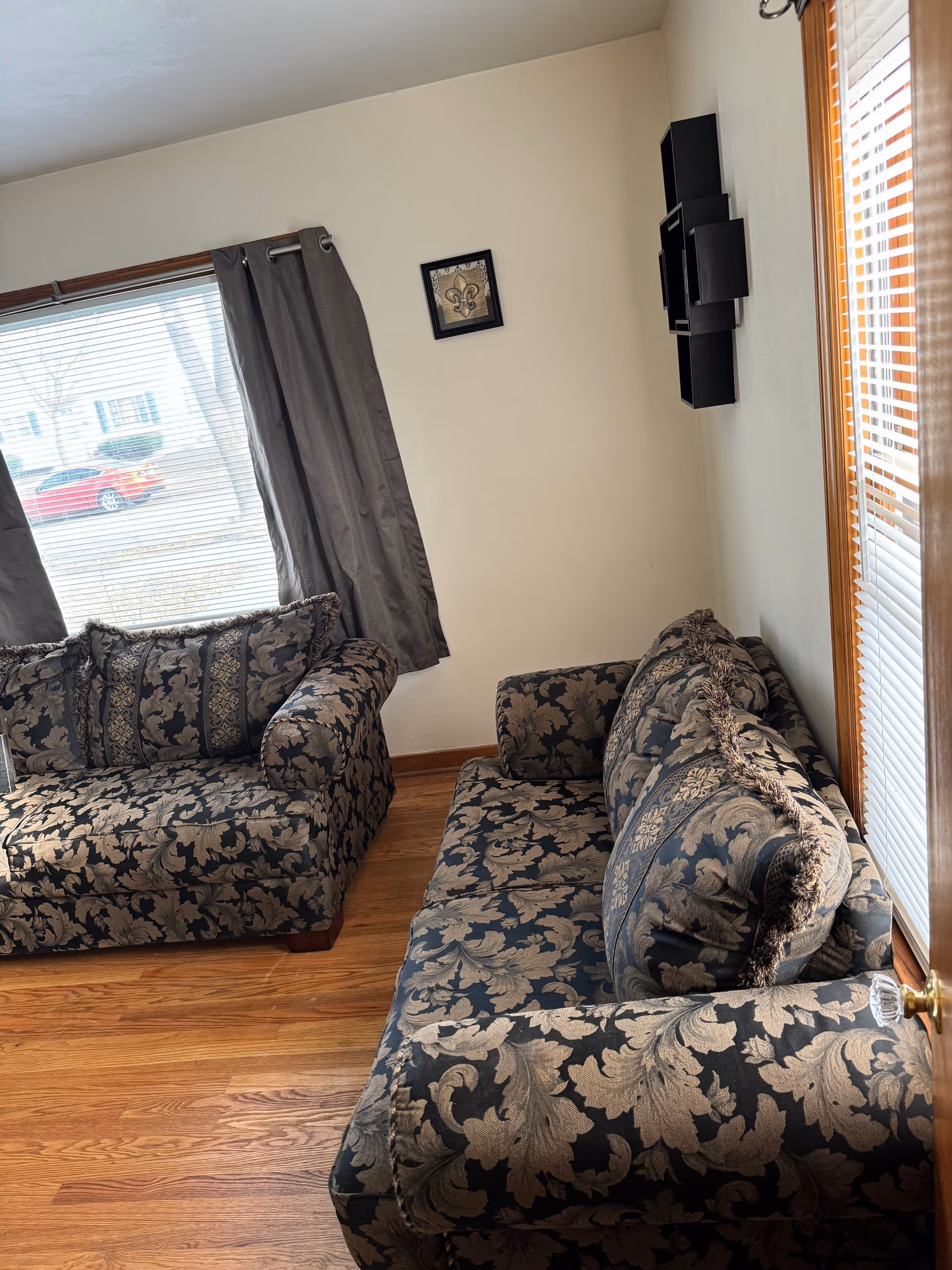 Floral-patterned living room with couches, windows, and wooden flooring.