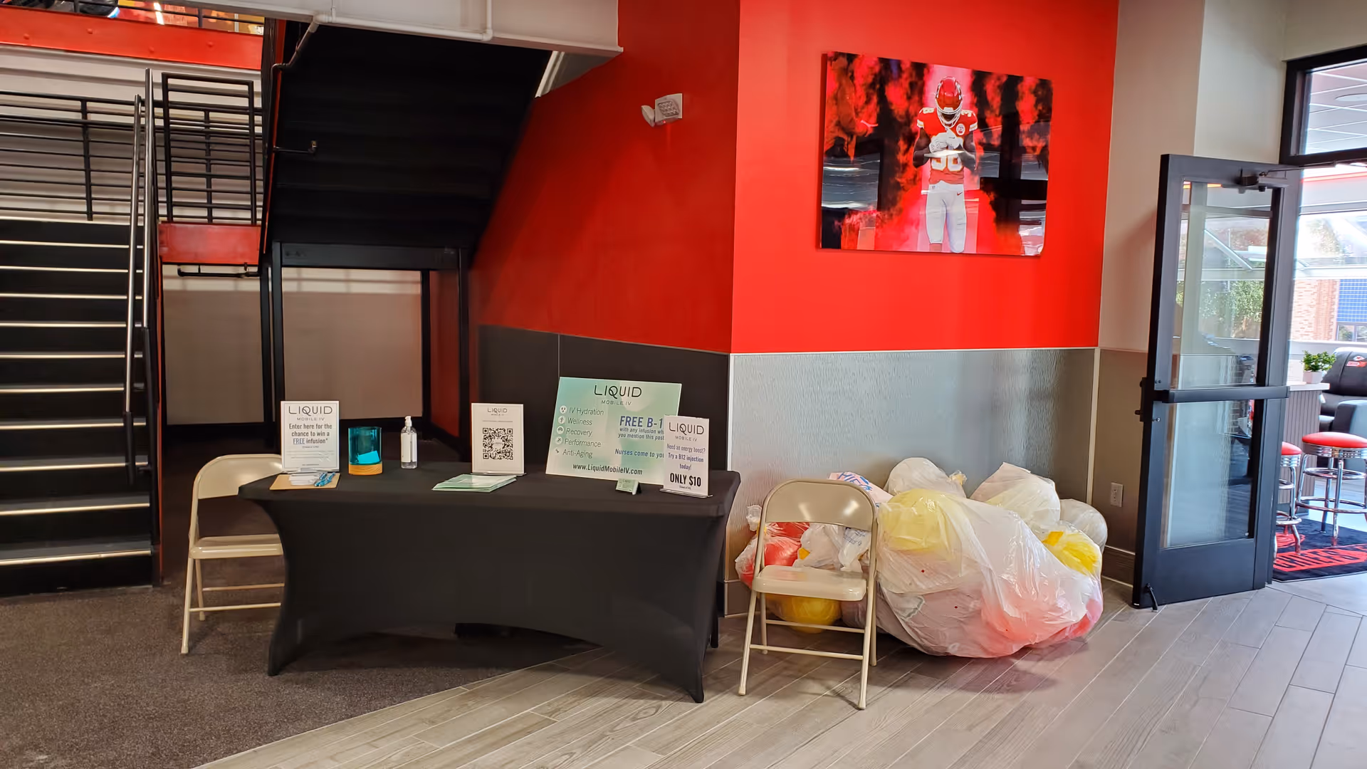Indoor facility lobby with a black table, red wall, staircase, and cluttered bags.