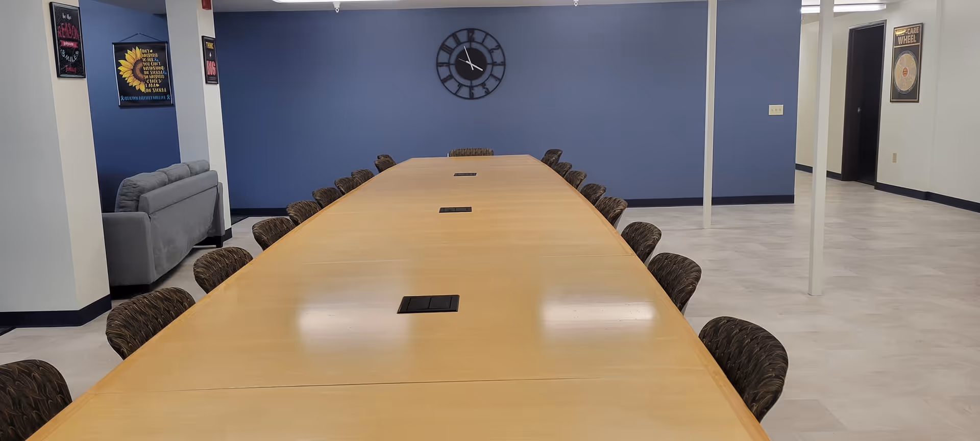 Long wooden conference table with chairs in a blue-walled empty indoor room.