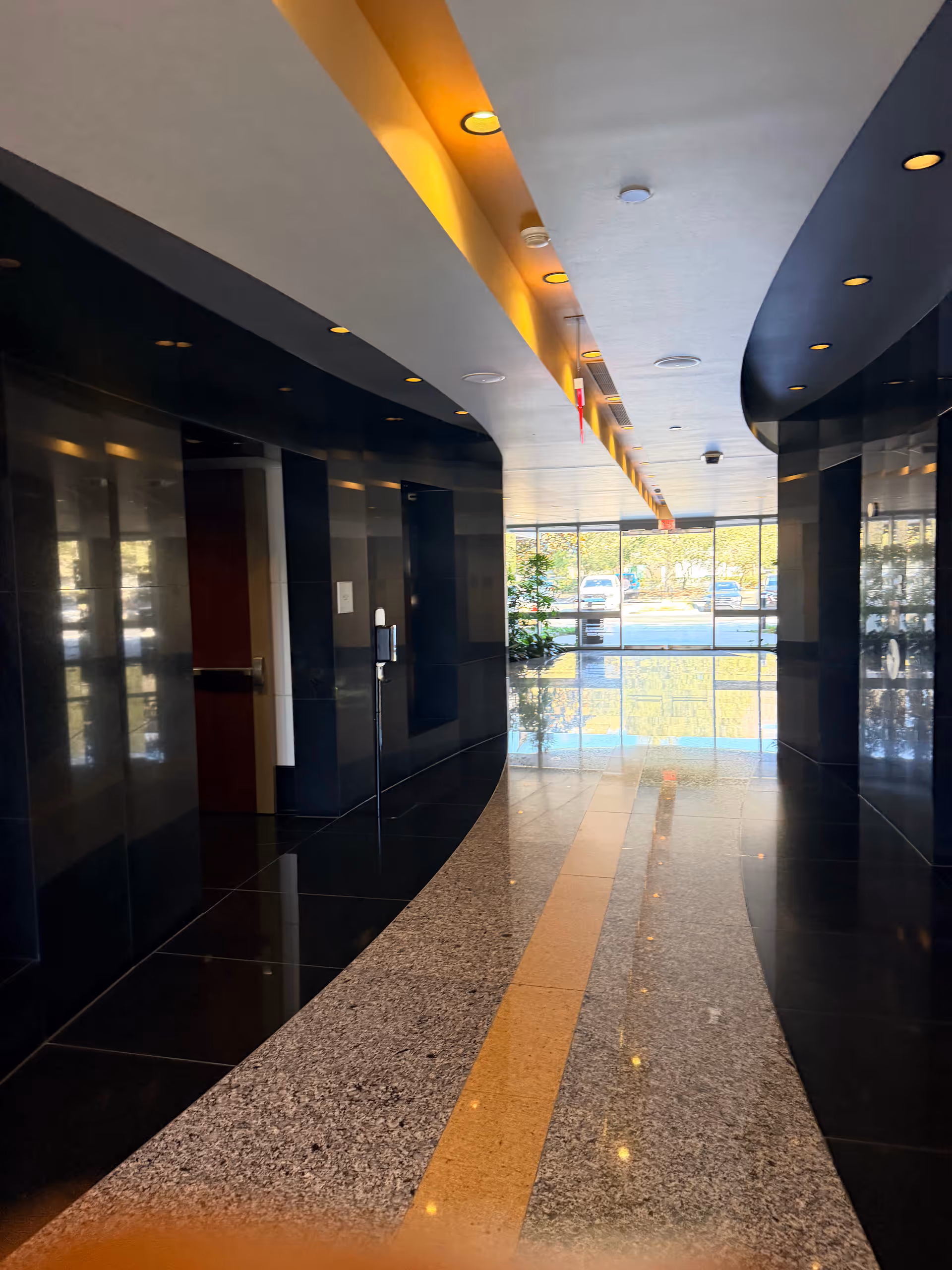 A polished modern hallway with dark walls, bright overhead lights, and glass doors at the end.