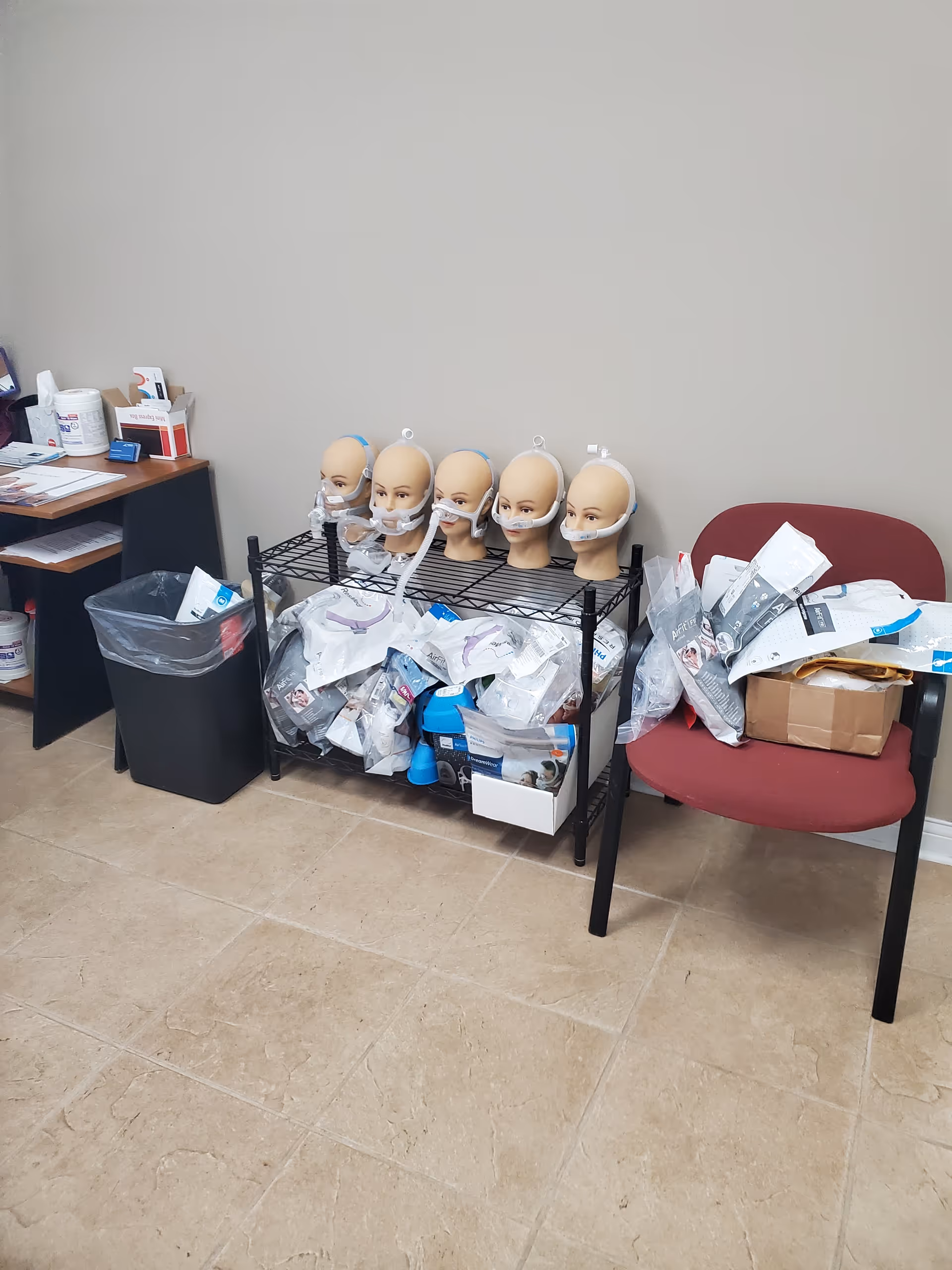 Row of mannequin heads with masks and scattered supplies on a metal shelf in a clinic