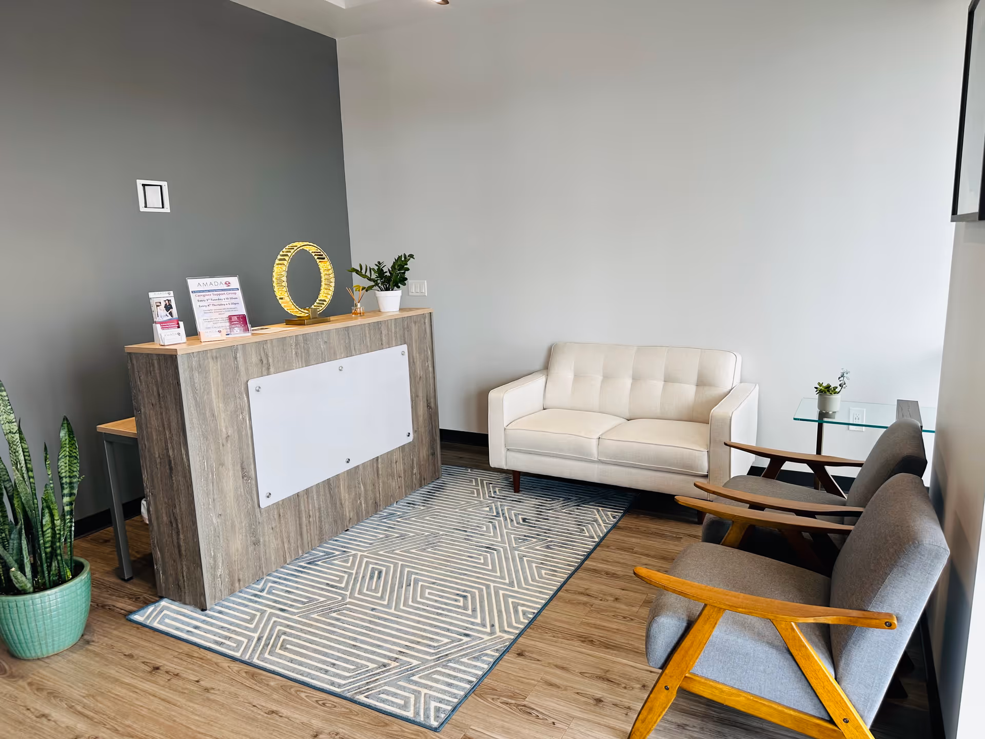 Modern interior lobby with reception desk, beige sofa, gray chairs, rug, and plants.