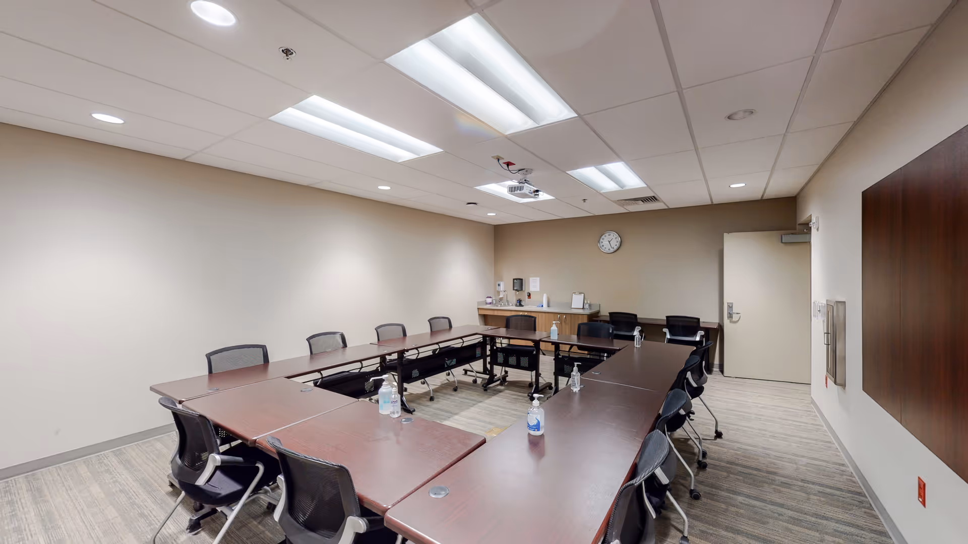 A large U-shaped conference table with chairs and sanitizer bottles in a well-lit meeting room.