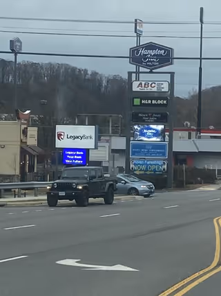 Street view with storefront signs, including Hampton Inn, along a busy road.