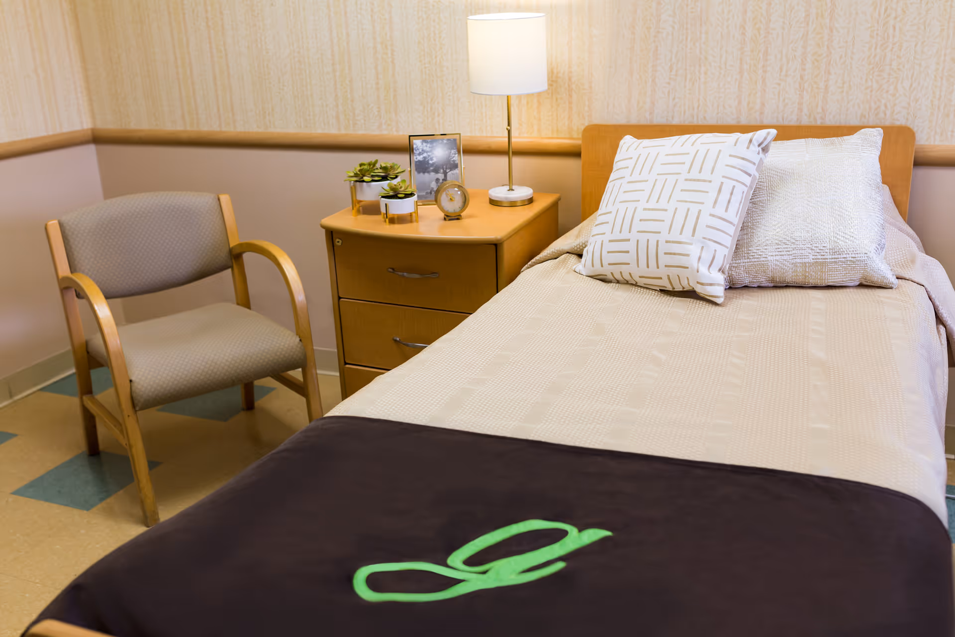 A furnished bedroom featuring a single bed, nightstand, lamp, chair, and decorative pillows.