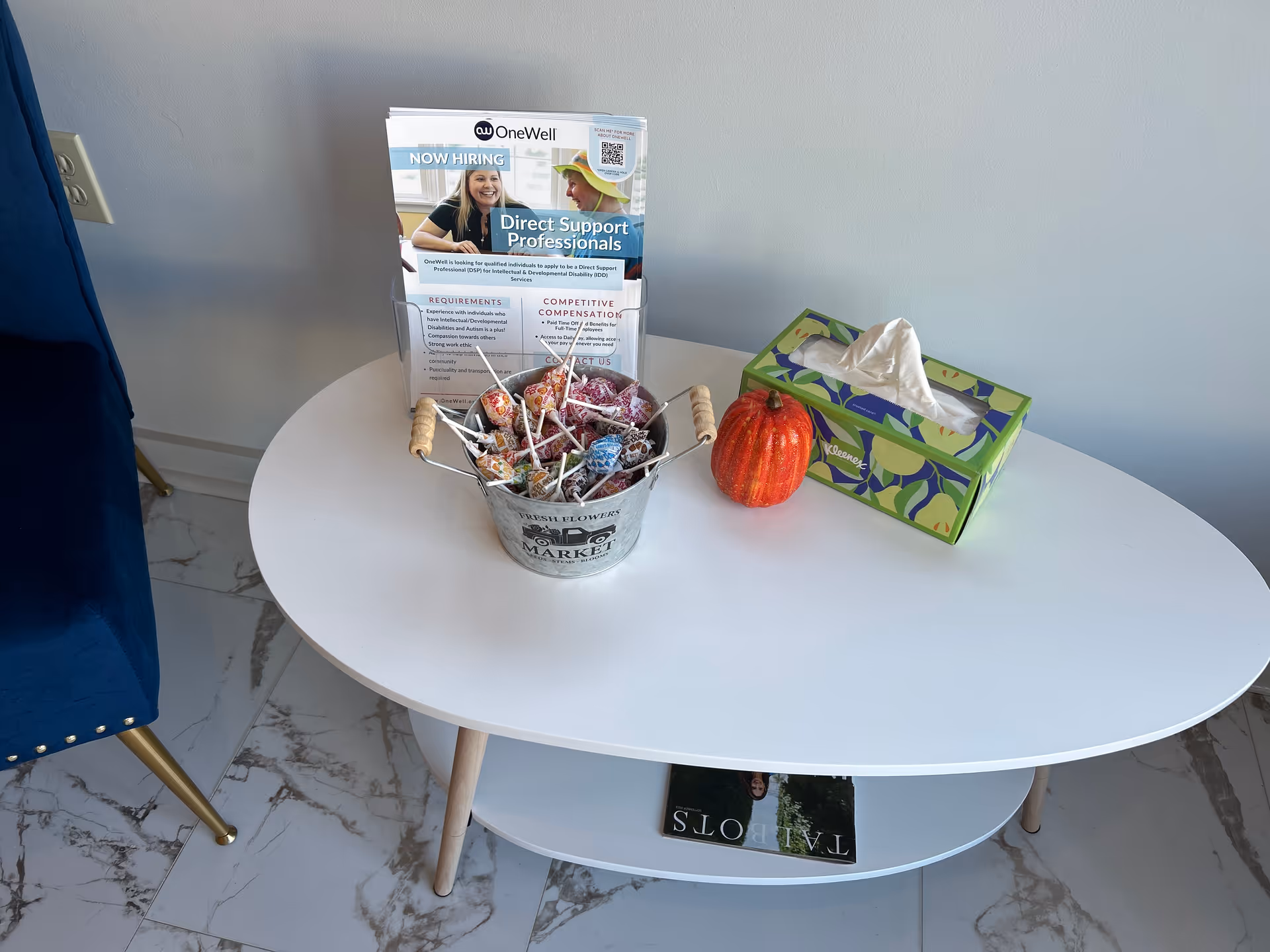 Round white table with candy bucket, pumpkin, tissue box, and brochure in a bright interior.