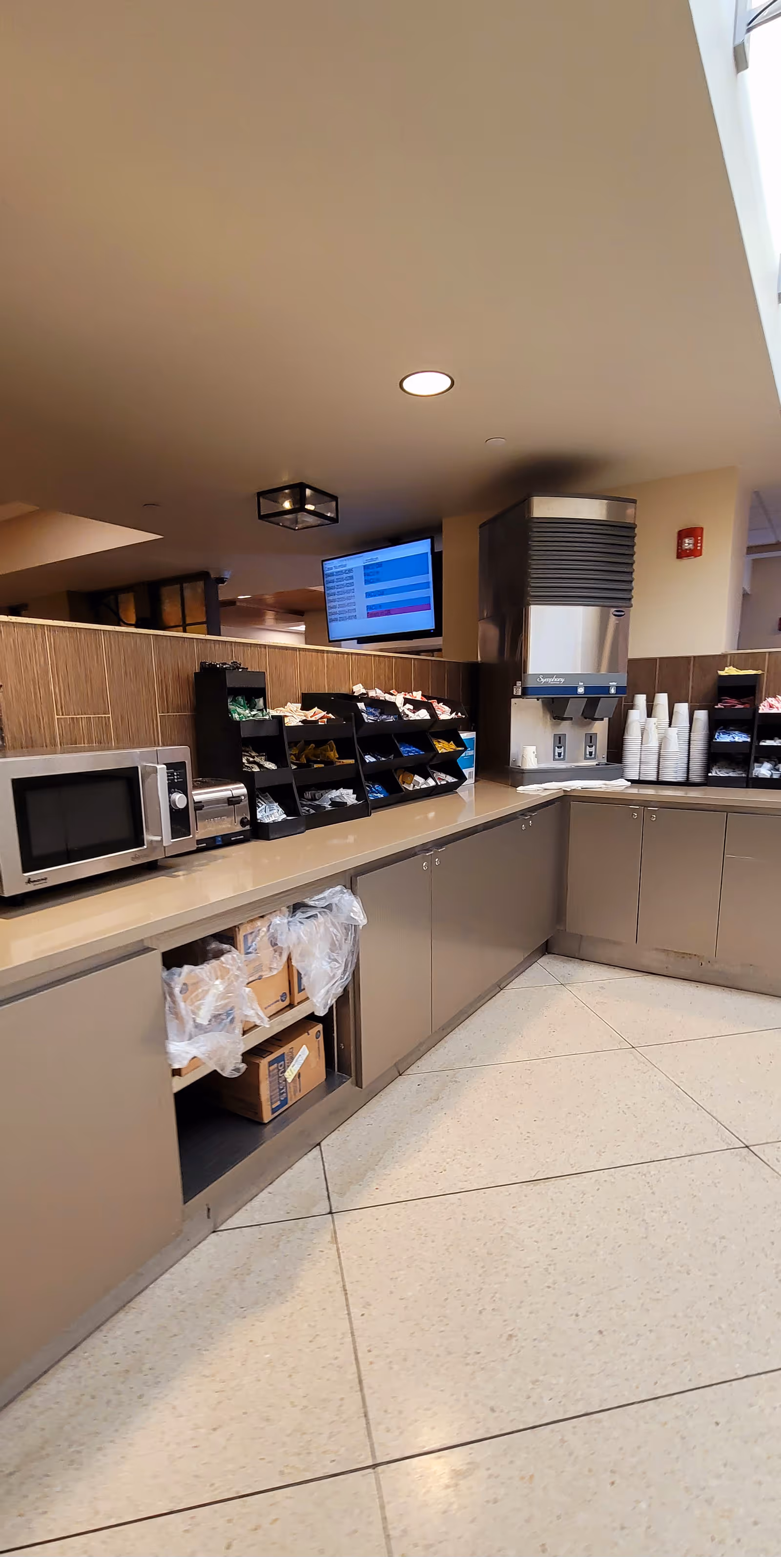 Senior living facility kitchenette with snack shelves, microwave, beverage station, and service counter.