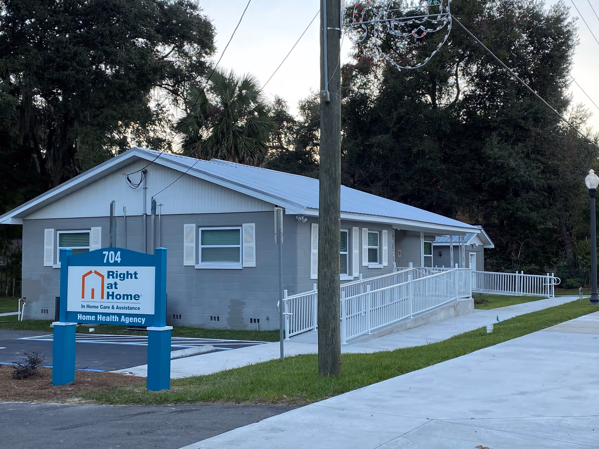Single-story gray facility with a blue Right at Home sign, wheelchair ramp and sidewalk.