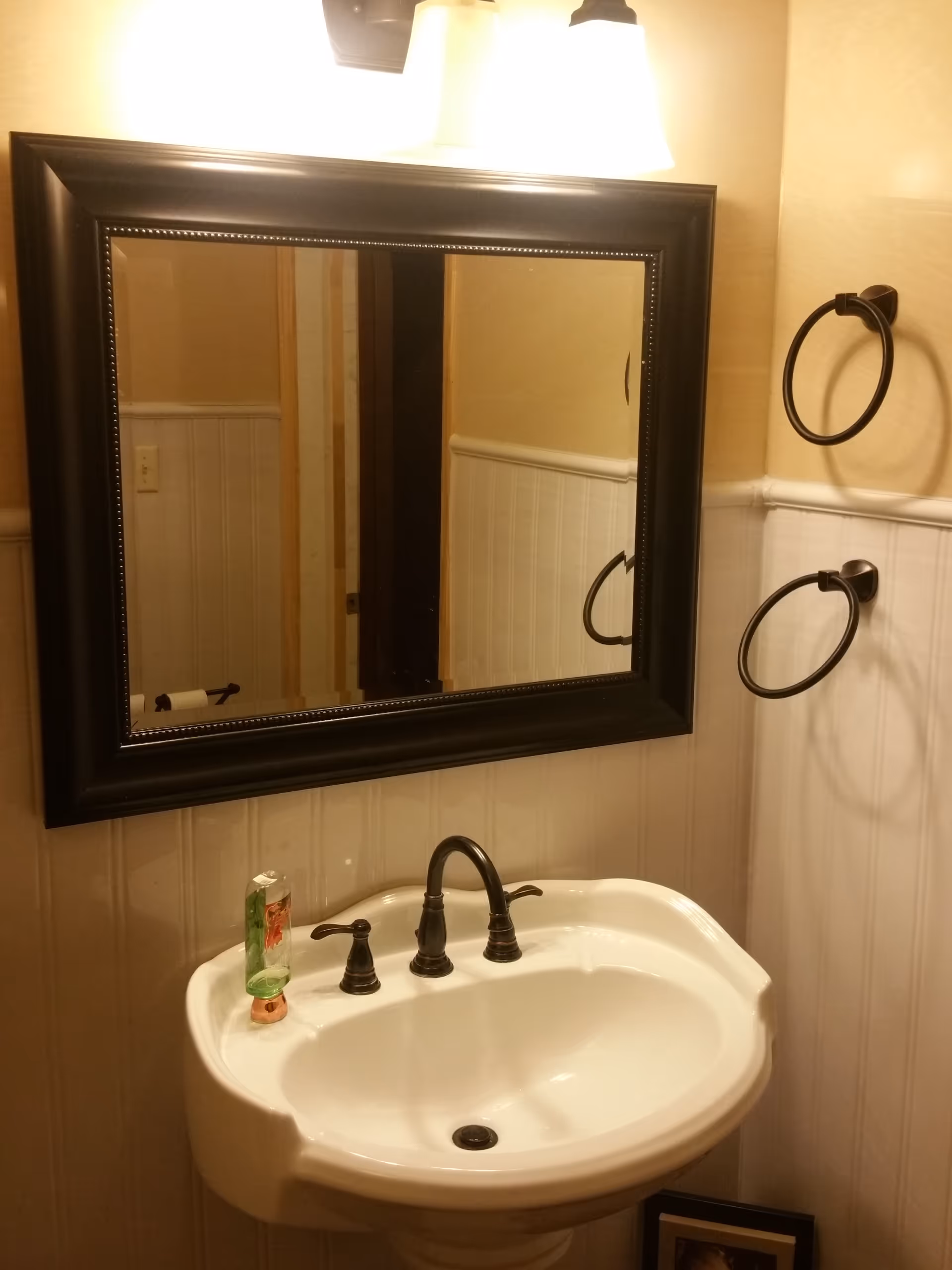 A bathroom sink with faucet, mirror, soap, and towel rings in beige-walled room.