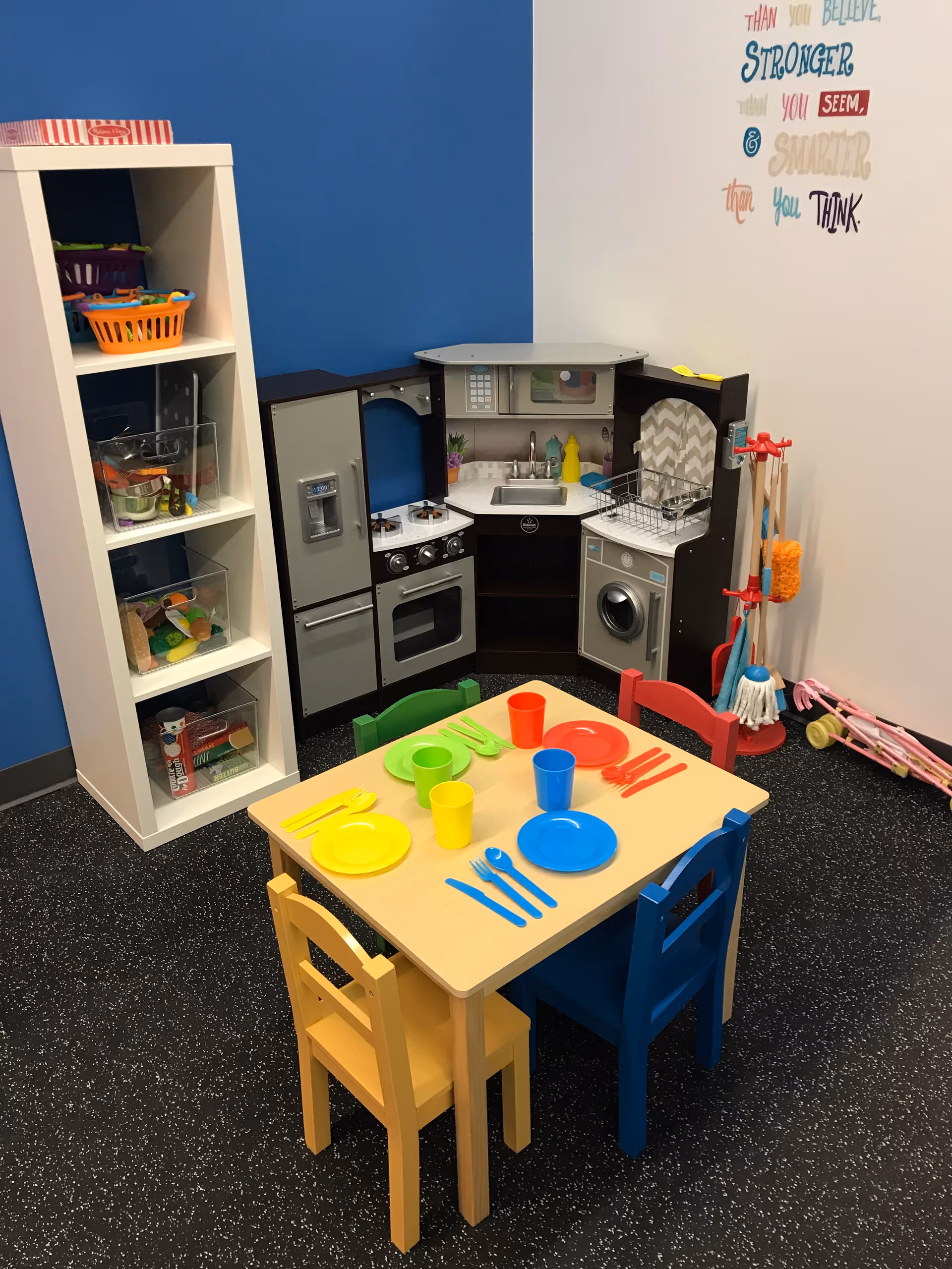 Bright playroom with colorful toy kitchen, table setting, and storage shelves.