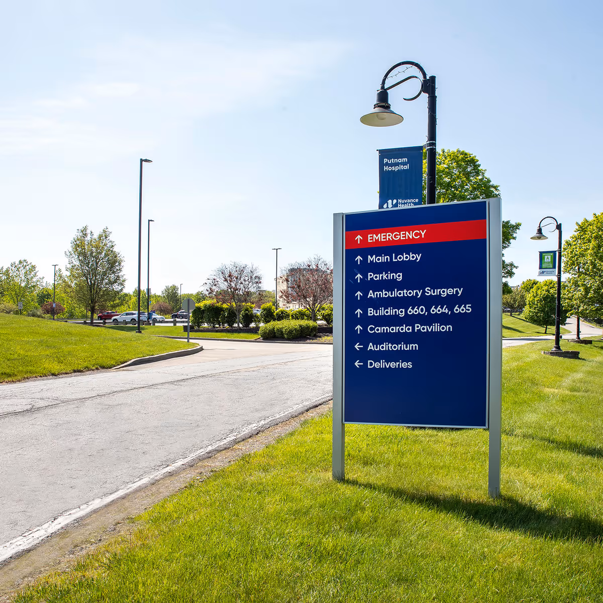 Blue outdoor hospital campus sign with directions to Emergency and services.