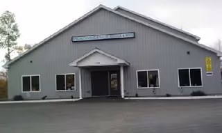 Gray single-story building with a central entrance and small windows, signage above doorway.
