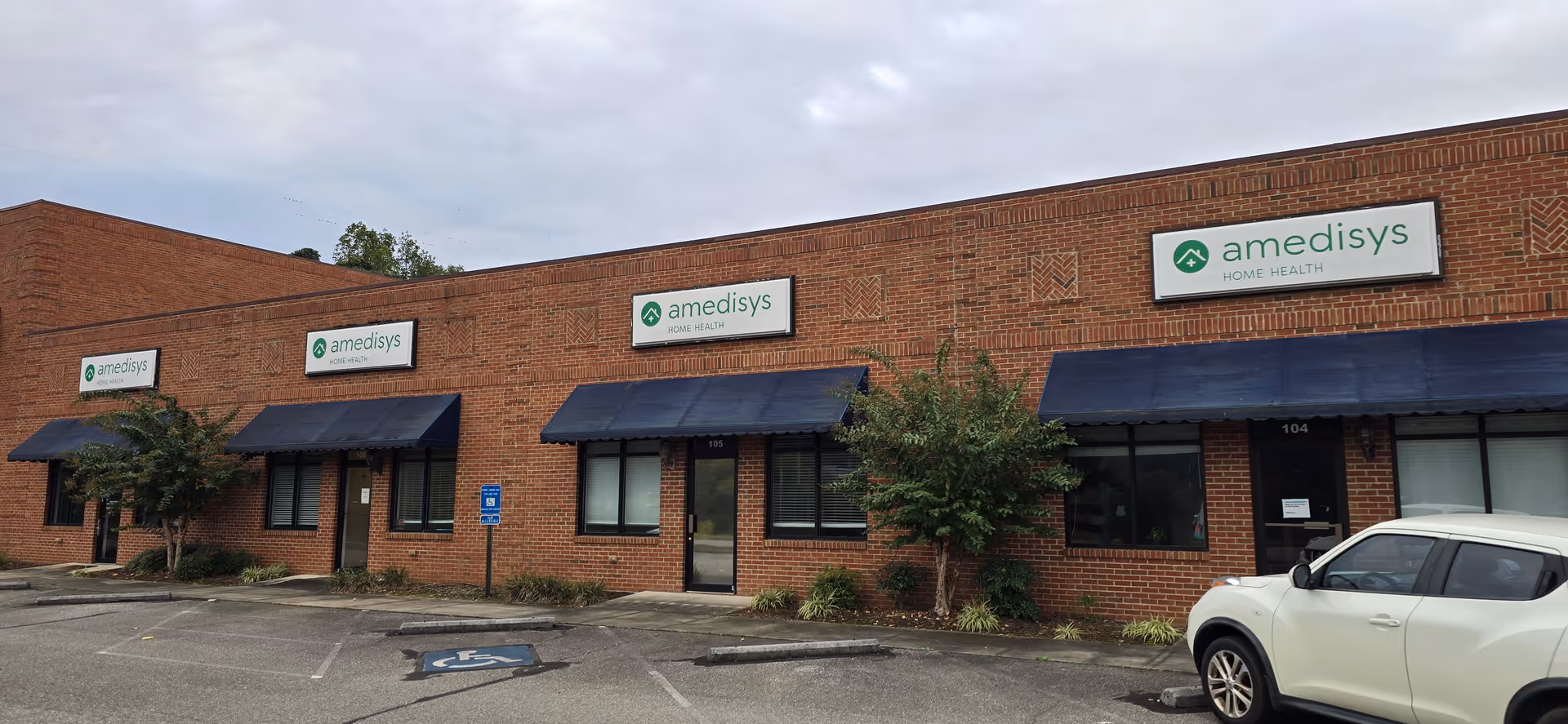 Brick exterior with storefronts, blue awnings, and Amedisys Home Health Care signs across the front.