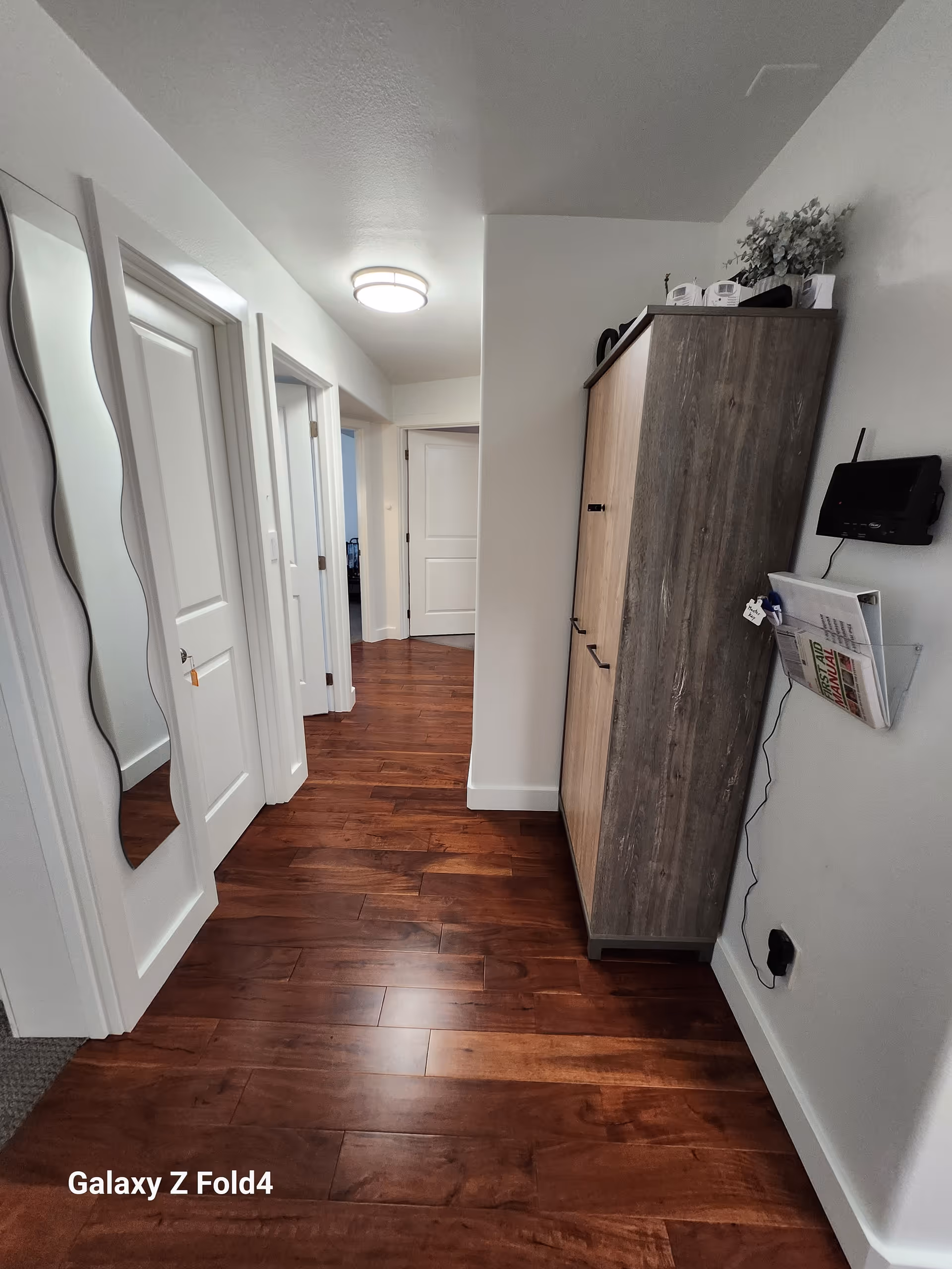Hallway in a senior living facility with wood floors, doors, a cabinet, and a mirror.