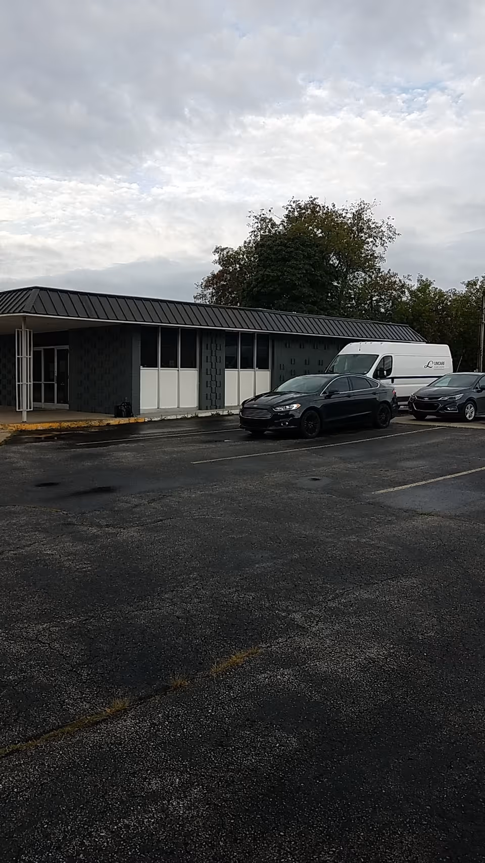 A single-story facility exterior with a LINCARE van and parked cars.