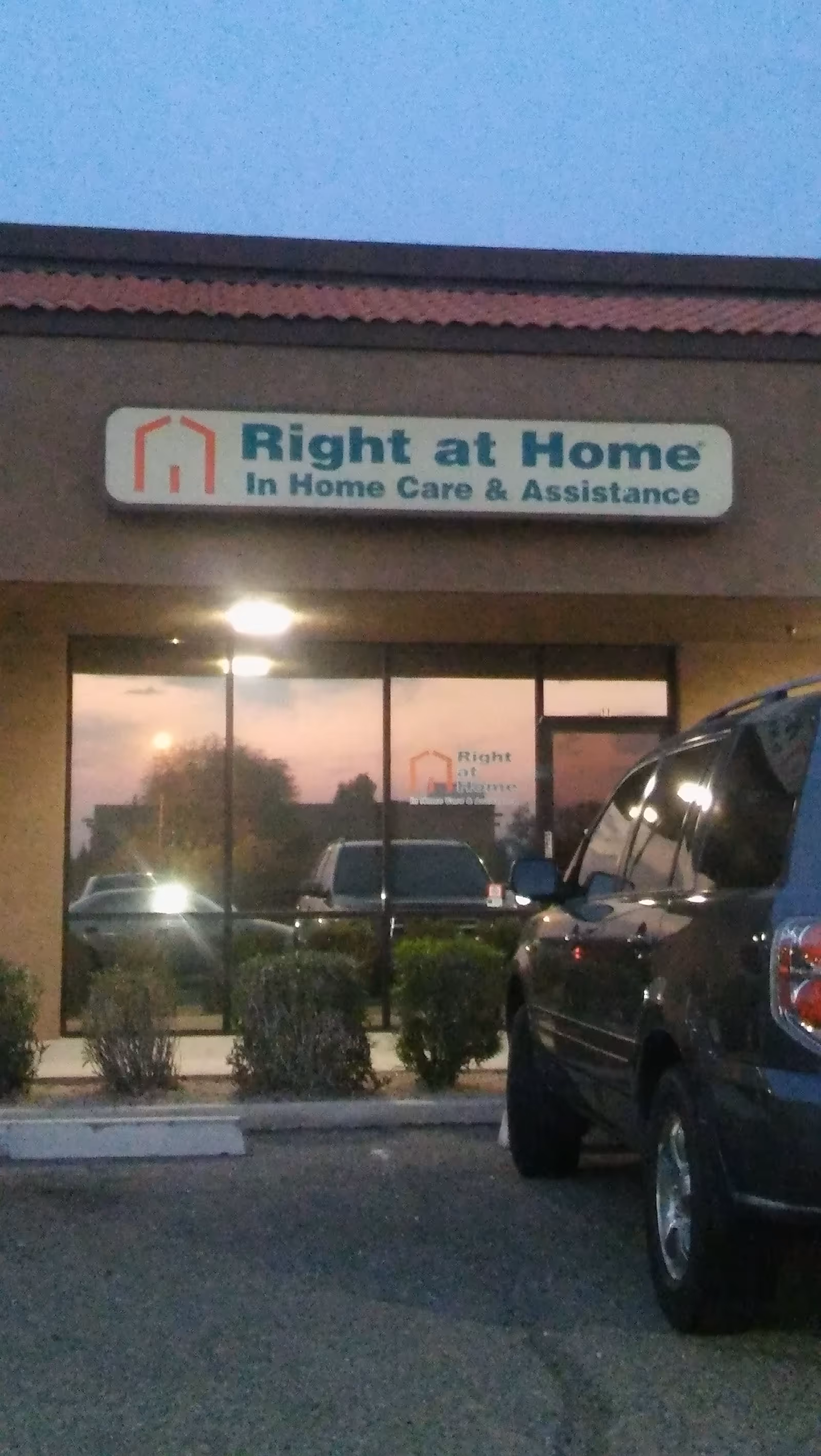 Exterior view of a Right at Home storefront with sign and parked vehicles in front.
