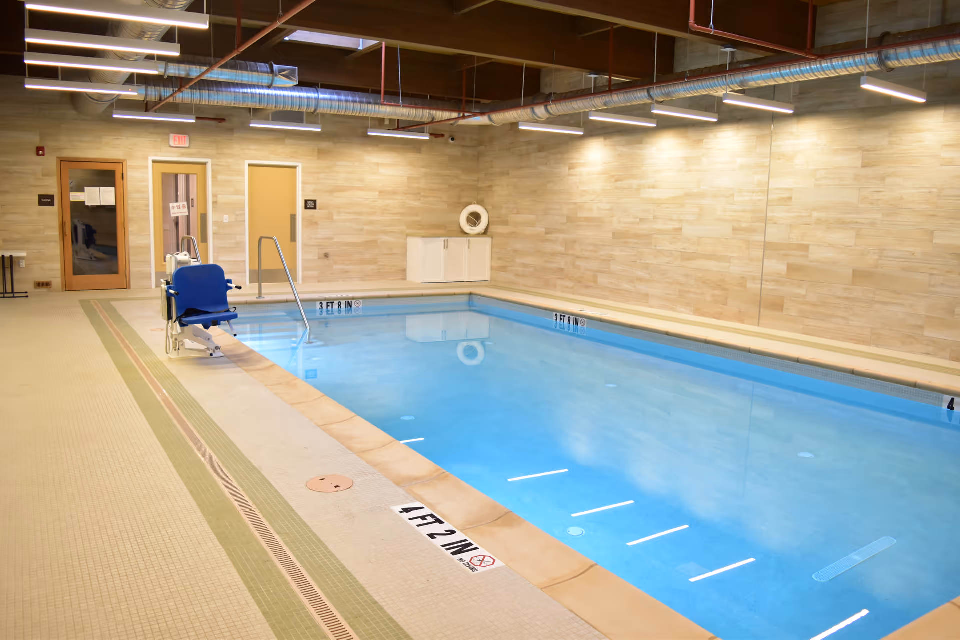 Indoor pool area with blue chair, pool water, and tiled walls.