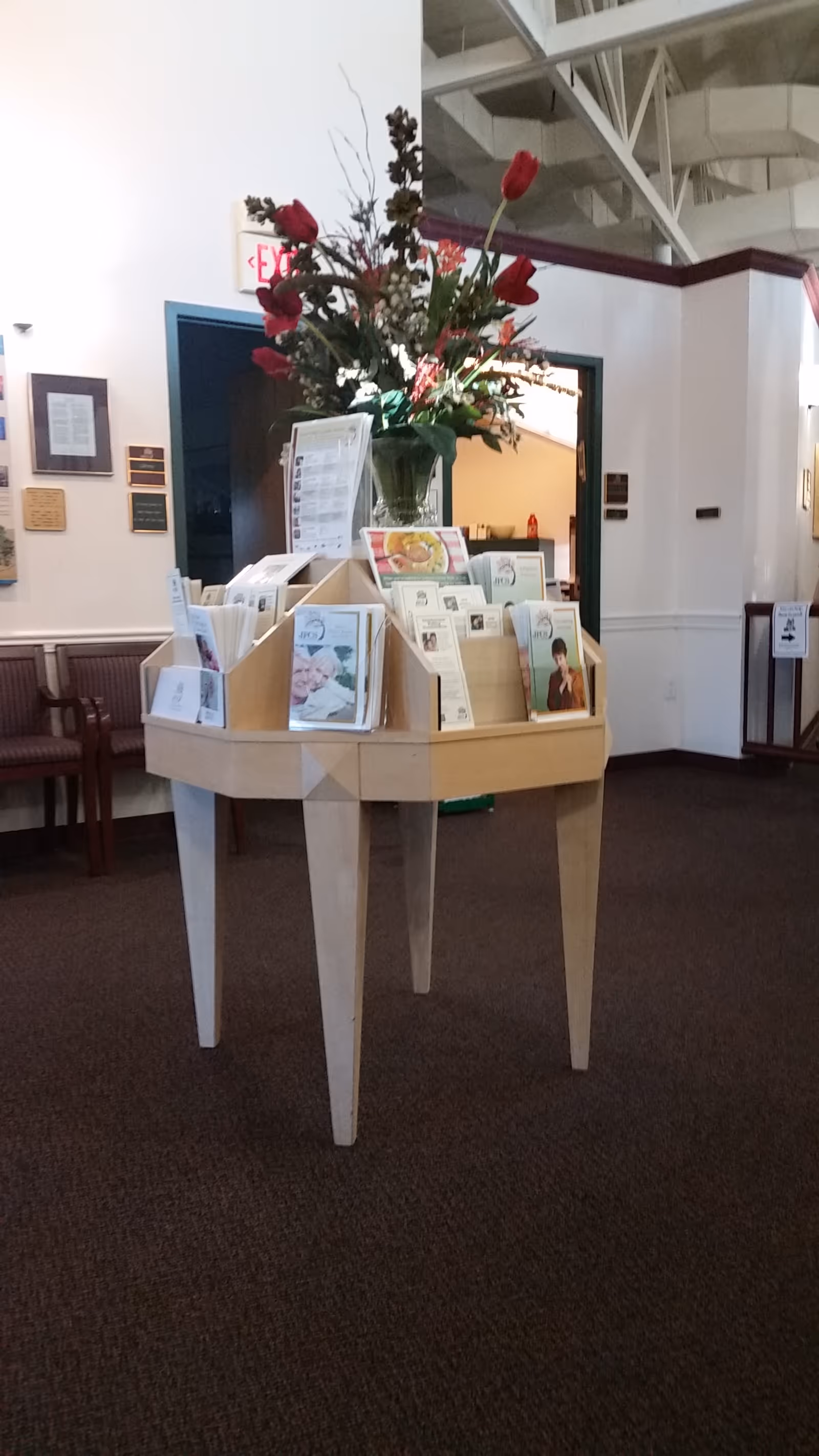 Lobby area with a magazine display table and flower arrangement inside a senior facility.