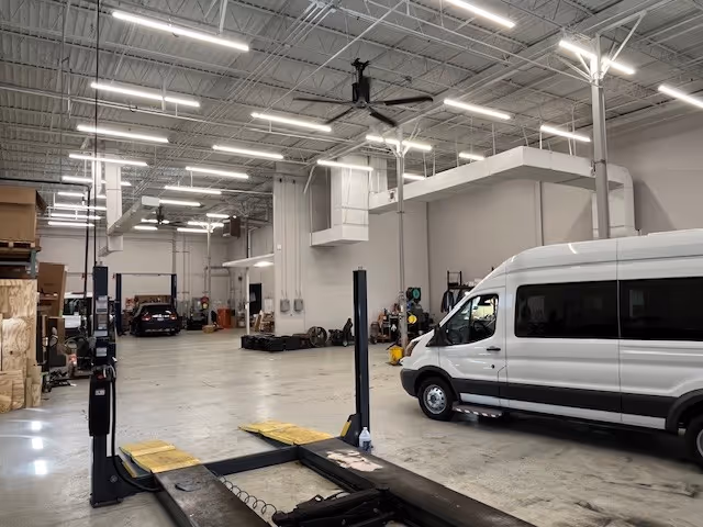 Inside a large, well-lit auto service area with a white mobility van and equipment.
