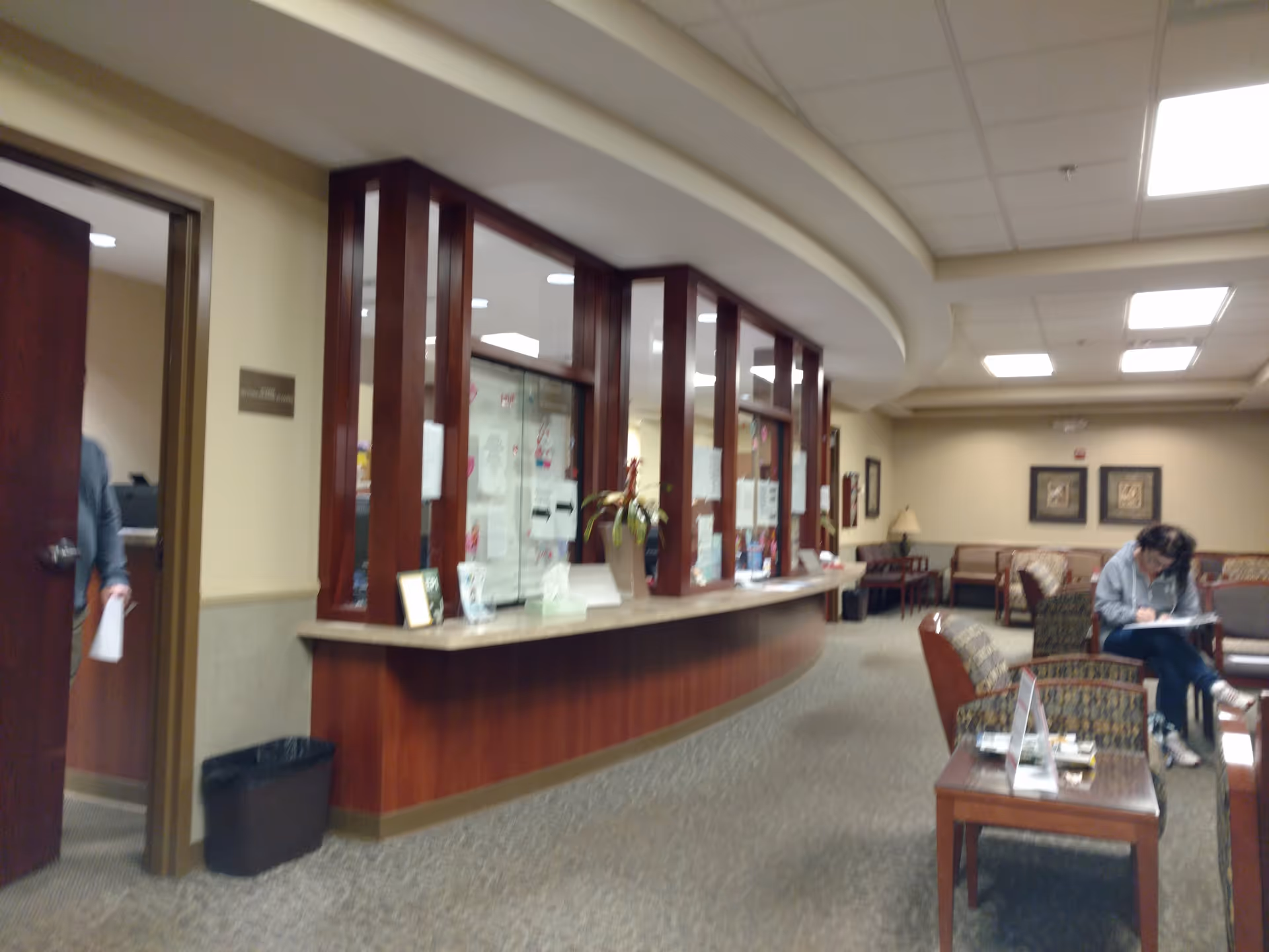 Curved wooden reception desk in a senior living lobby with seating.