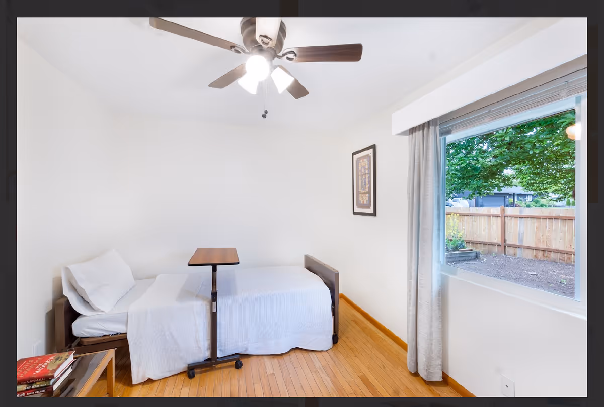 A small bedroom with a single bed, wheeled over-bed table, and a window.