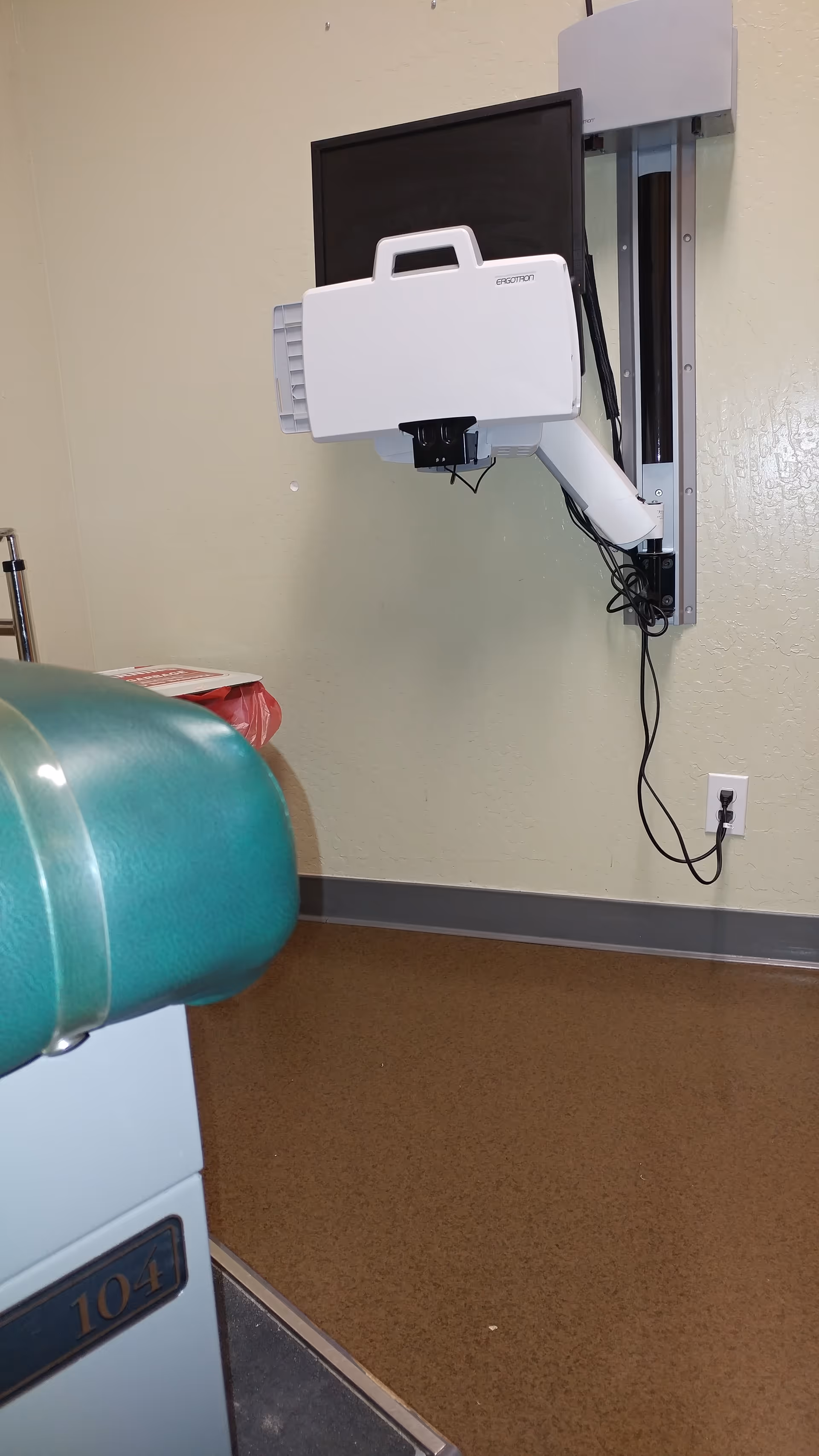 Wall-mounted medical imaging device with a monitor attached to the wall in a clinical room.