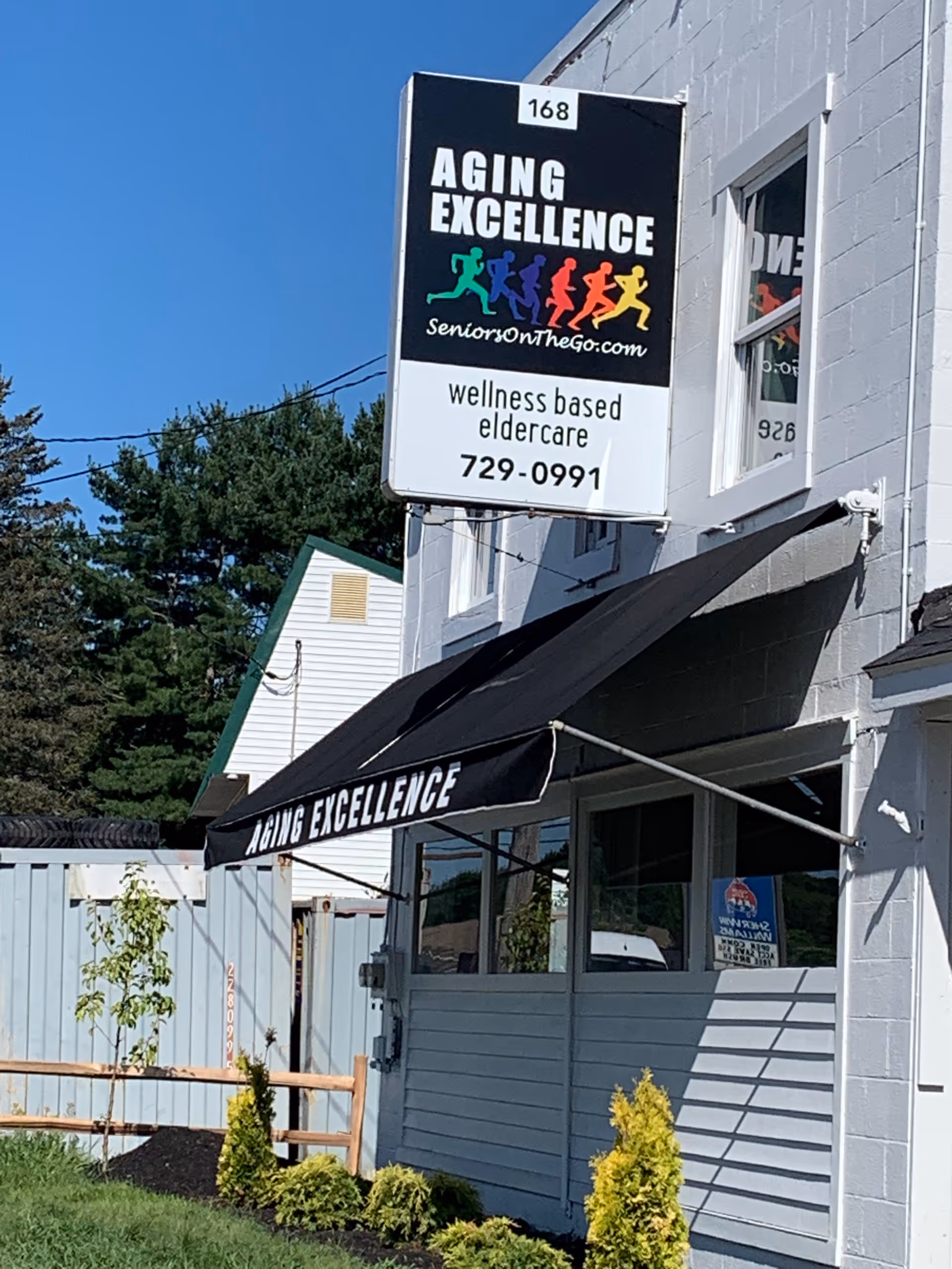 Exterior view of Aging Excellence building with front sign and black awning storefront.
