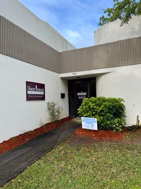Entrance to Home Instead Senior Care facility with a pathway, shrubs, and a sign.