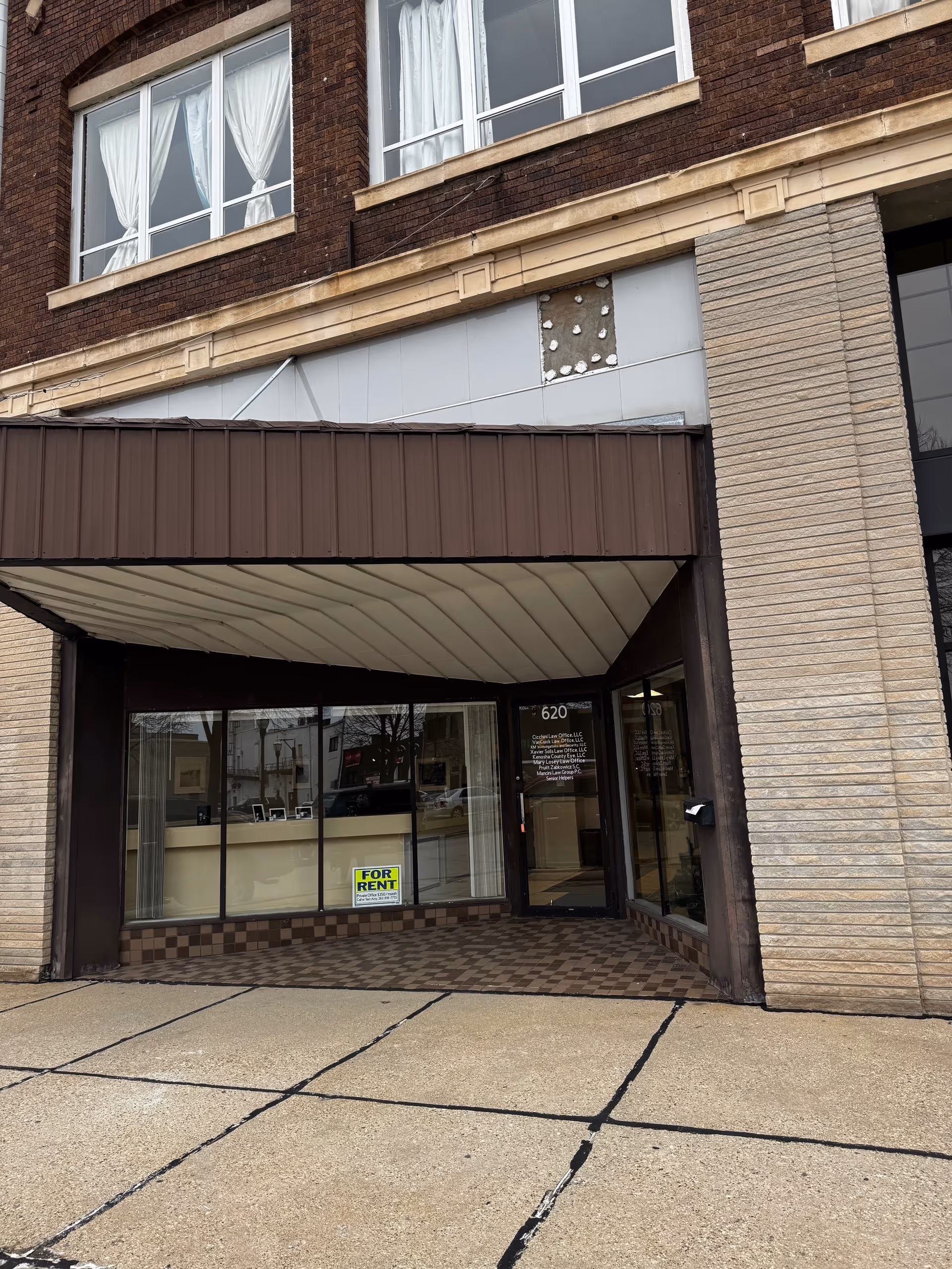 Brick building exterior with brown awning and large glass storefront.