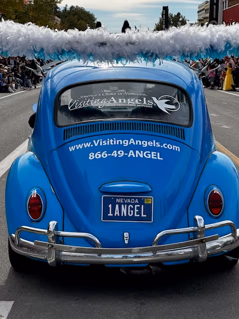 Blue vintage car on a city street advertising Visiting Angels Senior Home Care.
