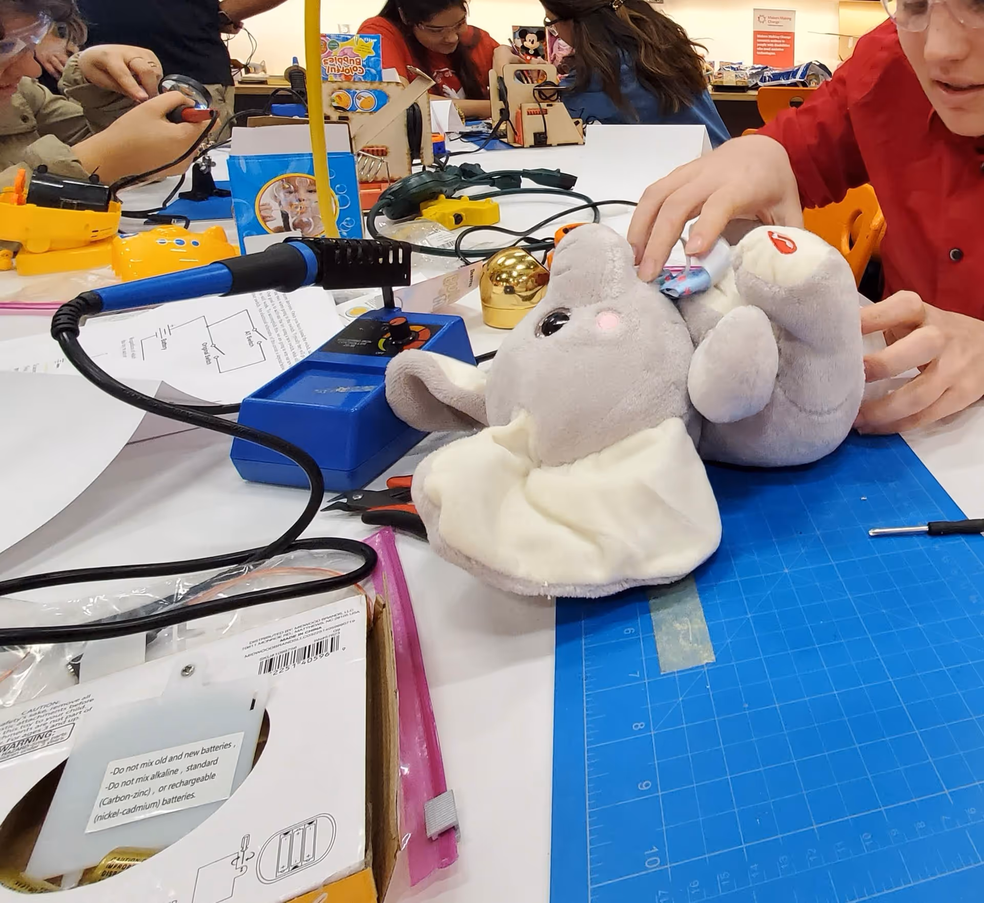 Indoor craft activity at a table with plush elephants and tools.