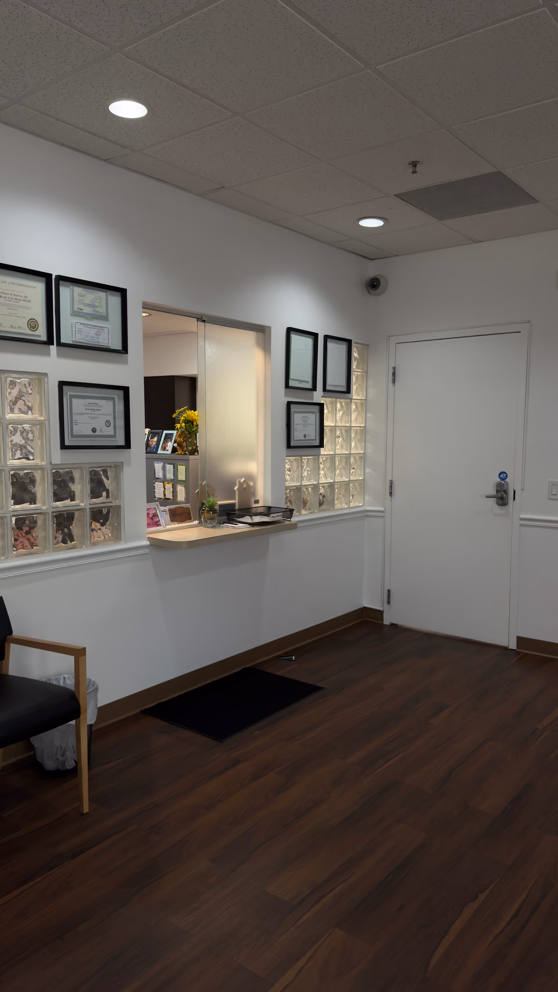 Interior reception area with framed certificates, a counter, and a door along white walls.