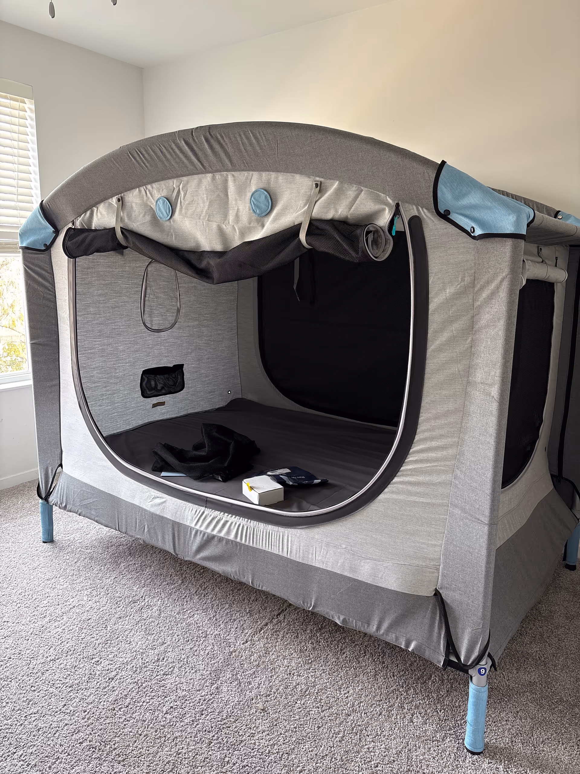 Gray portable tent structure set up inside a carpeted room near a window.