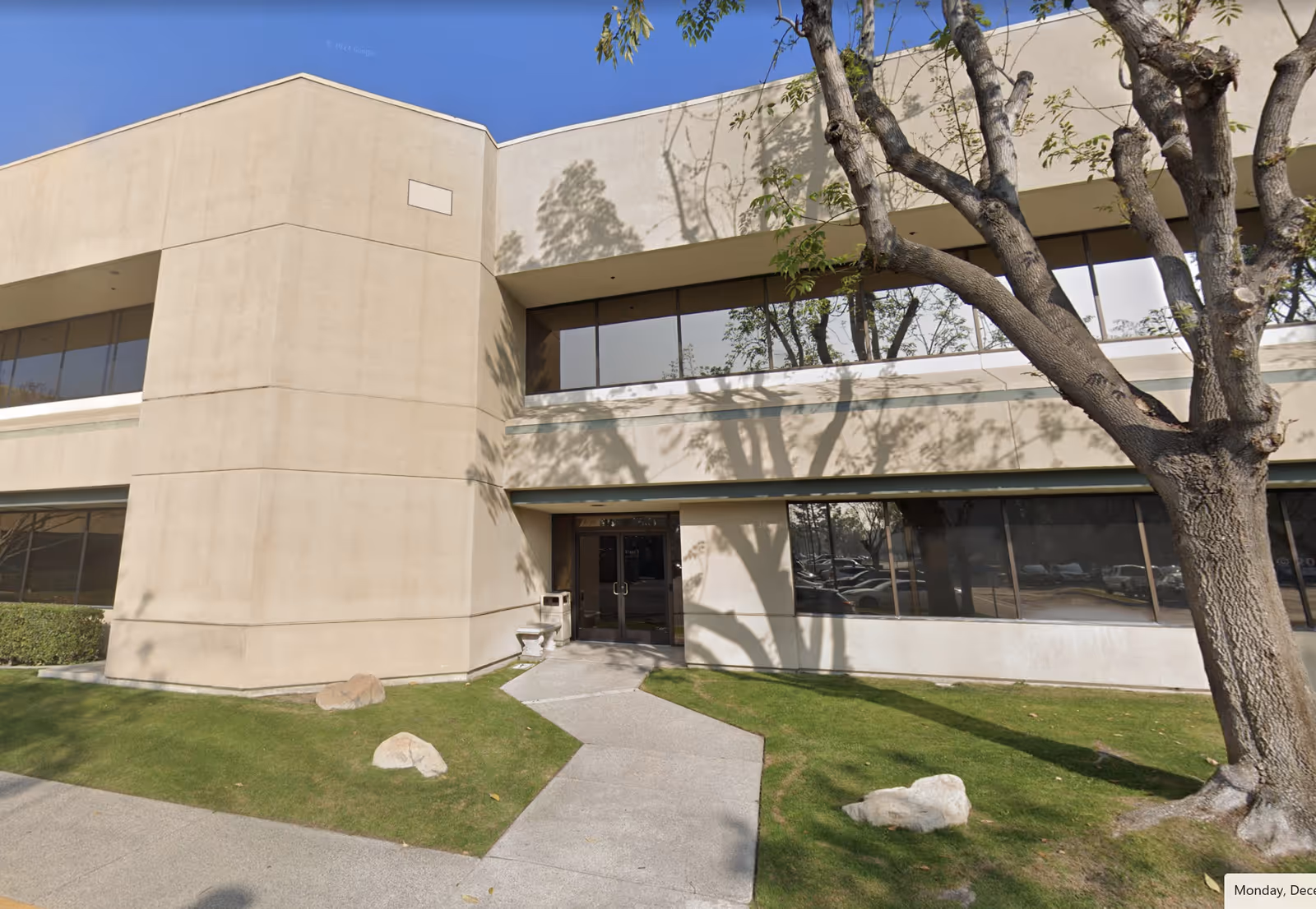 Beige two-story Allied Home Care facility exterior with large windows, entryway, walkway, and tree.