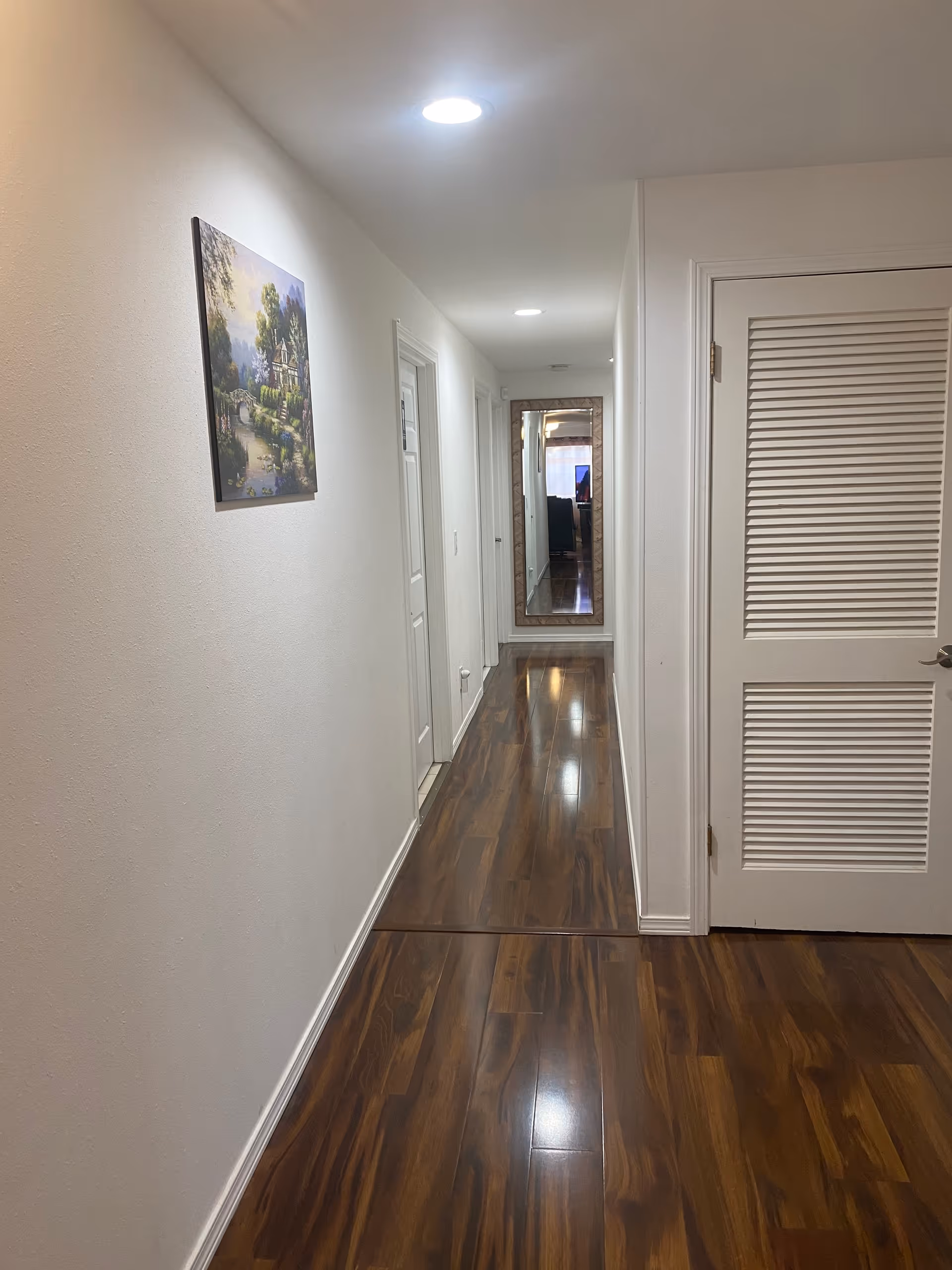 Bright hallway of a senior living facility with white walls, doors, and a full-length mirror.