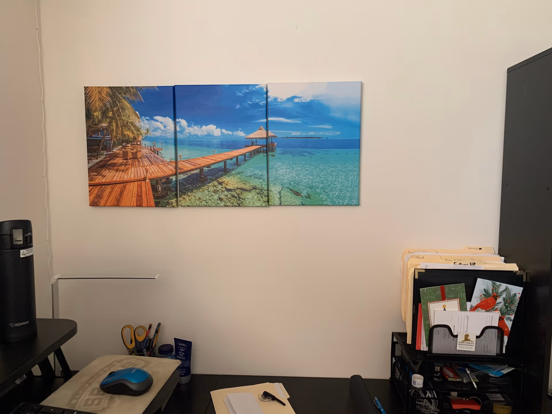 Office desk area with beach-themed art and filing supplies.