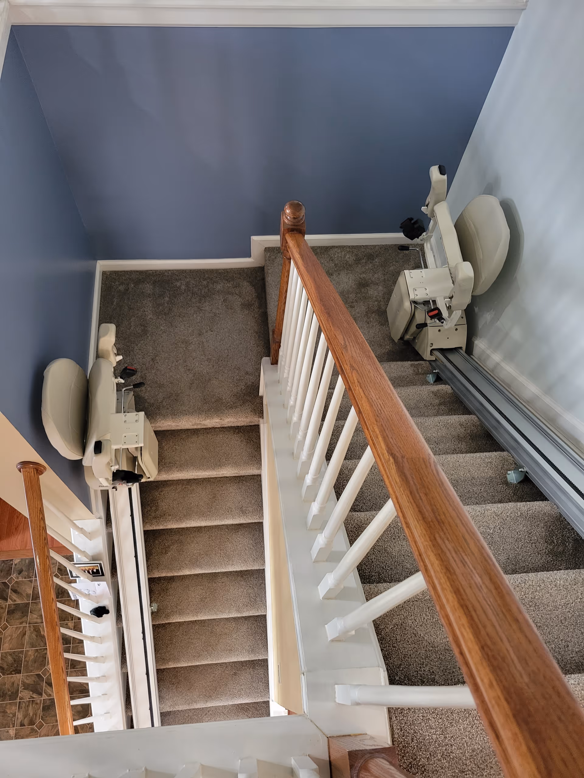 Top-down view of carpeted interior stairs with dual chairlifts along a blue-walled stairwell.