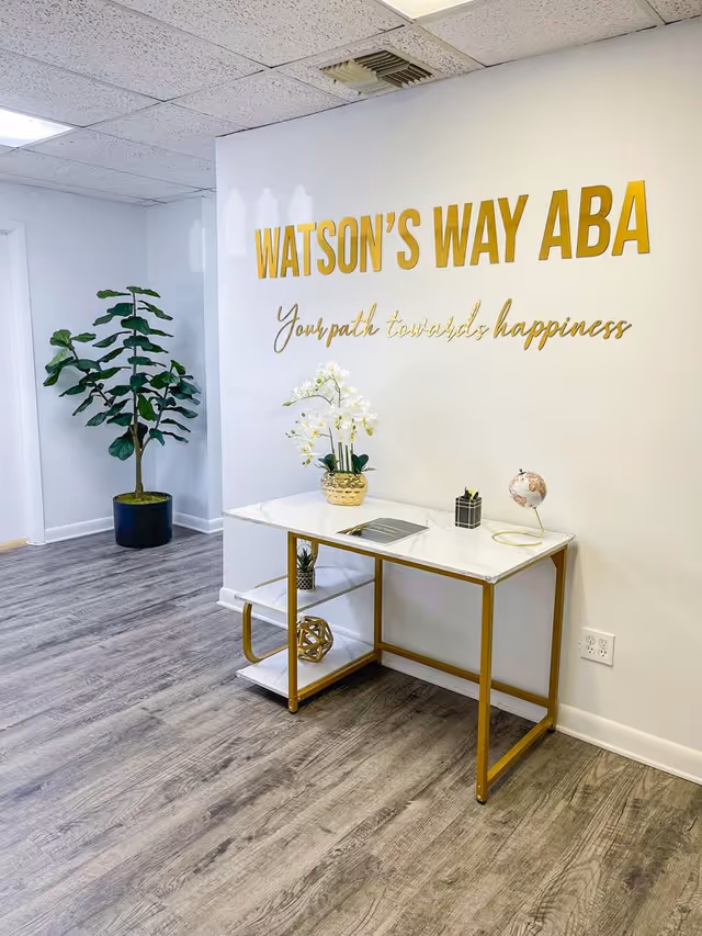 Interior hallway with a Watson's Way ABA sign, console table, and potted plants.