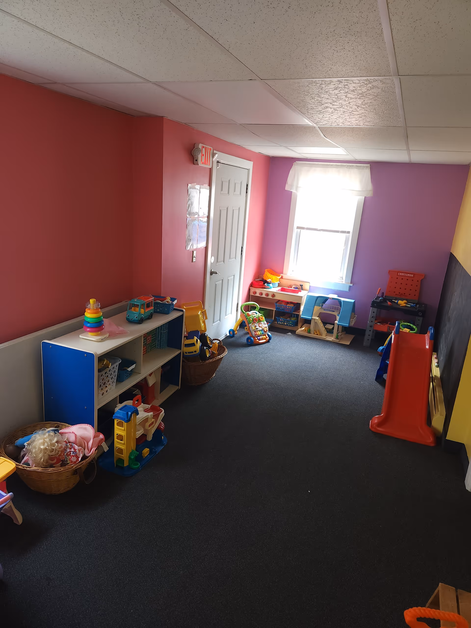 Colorful children's playroom with shelves, toys, and a small red slide.