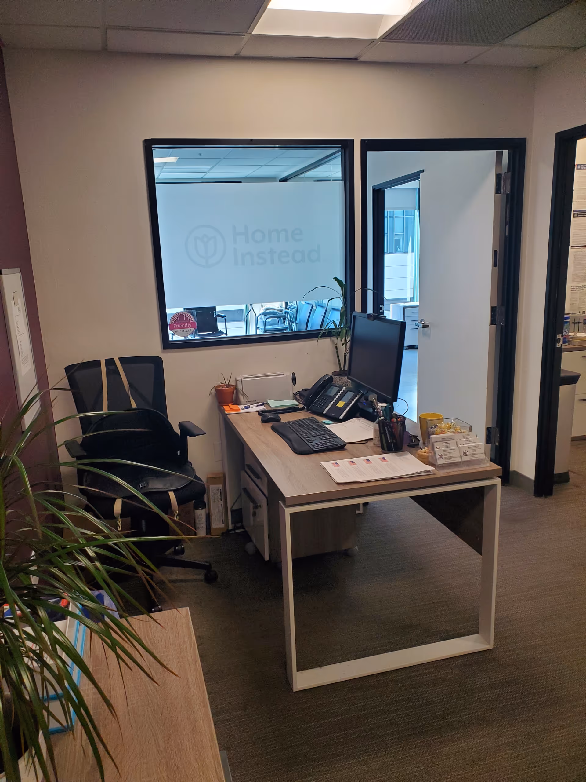 Desk with computer, phone, and plant inside a Home Instead office.