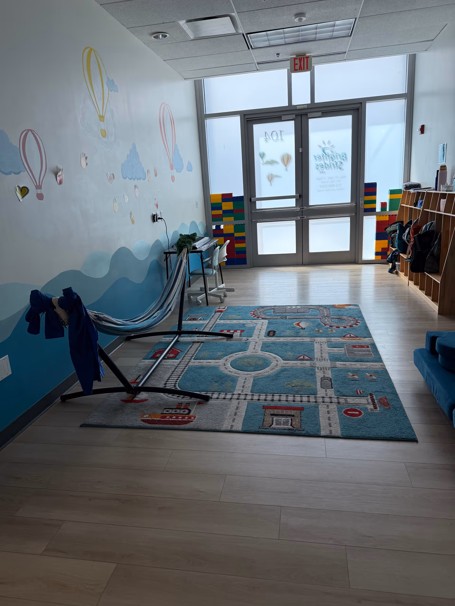 Bright interior with mural walls, a road-themed rug, and therapy equipment near exit.