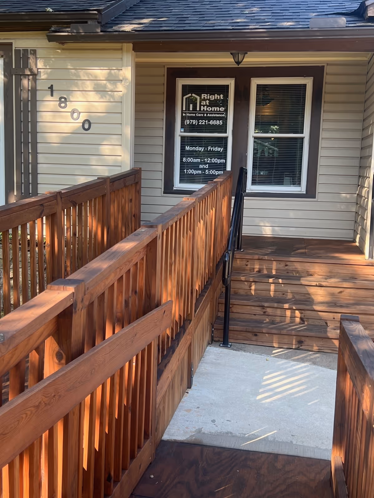 Wooden ramp leads to a beige exterior entrance with a sign for Right at Home.
