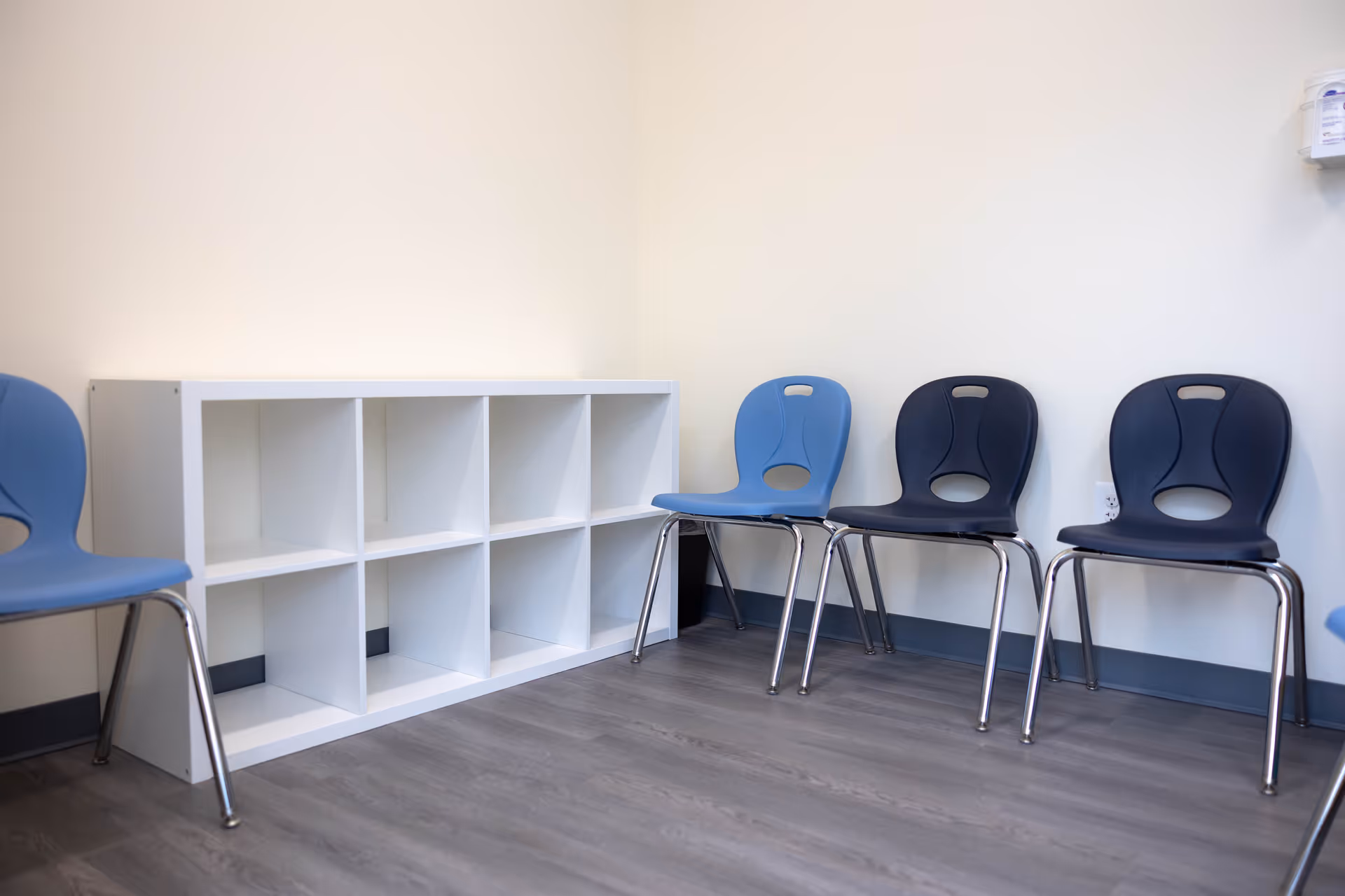 A small waiting area with blue chairs along the wall and white cubby shelves.
