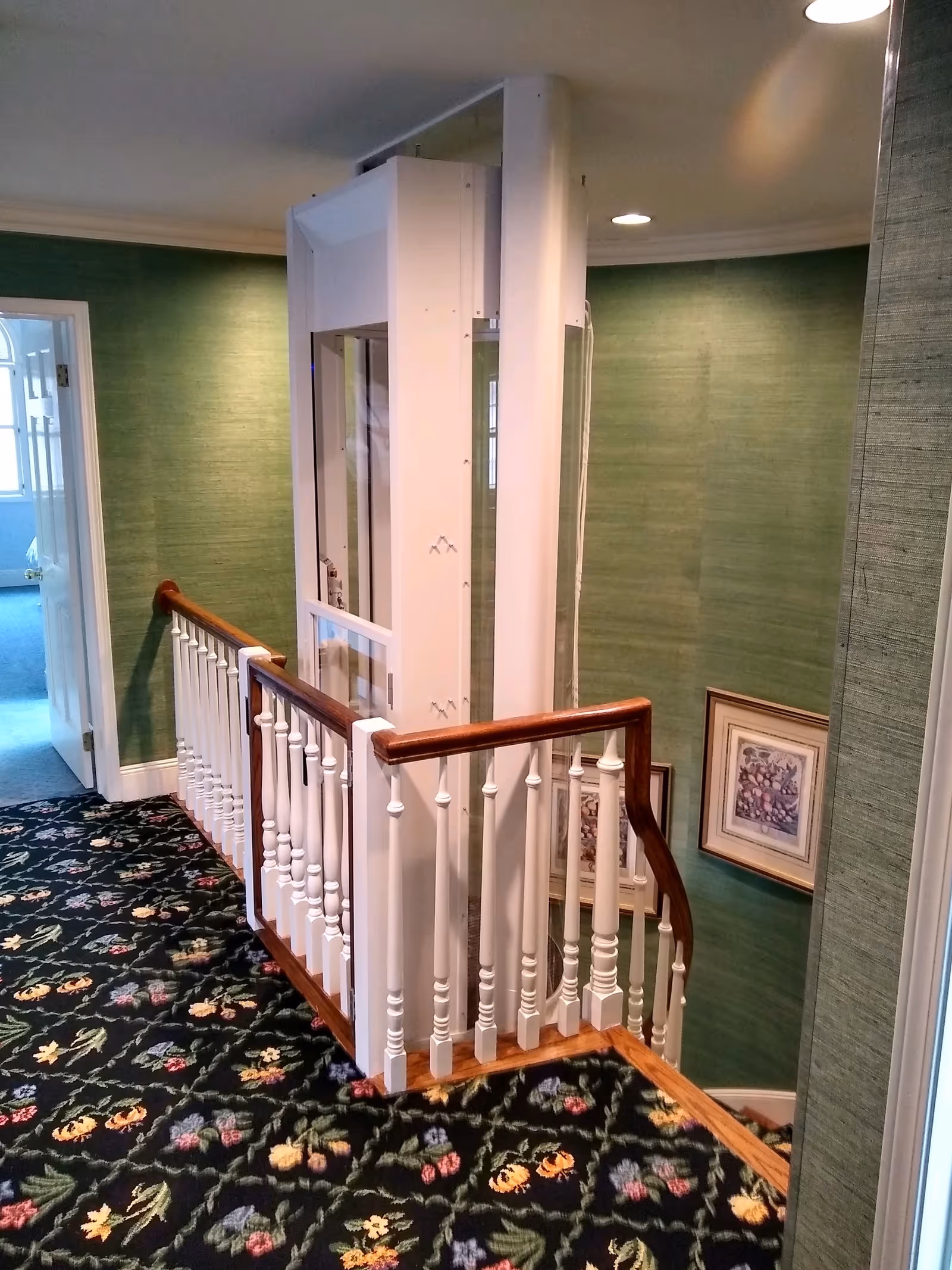 Interior stairwell with white railing, floral carpet, green walls, and a central elevator shaft.