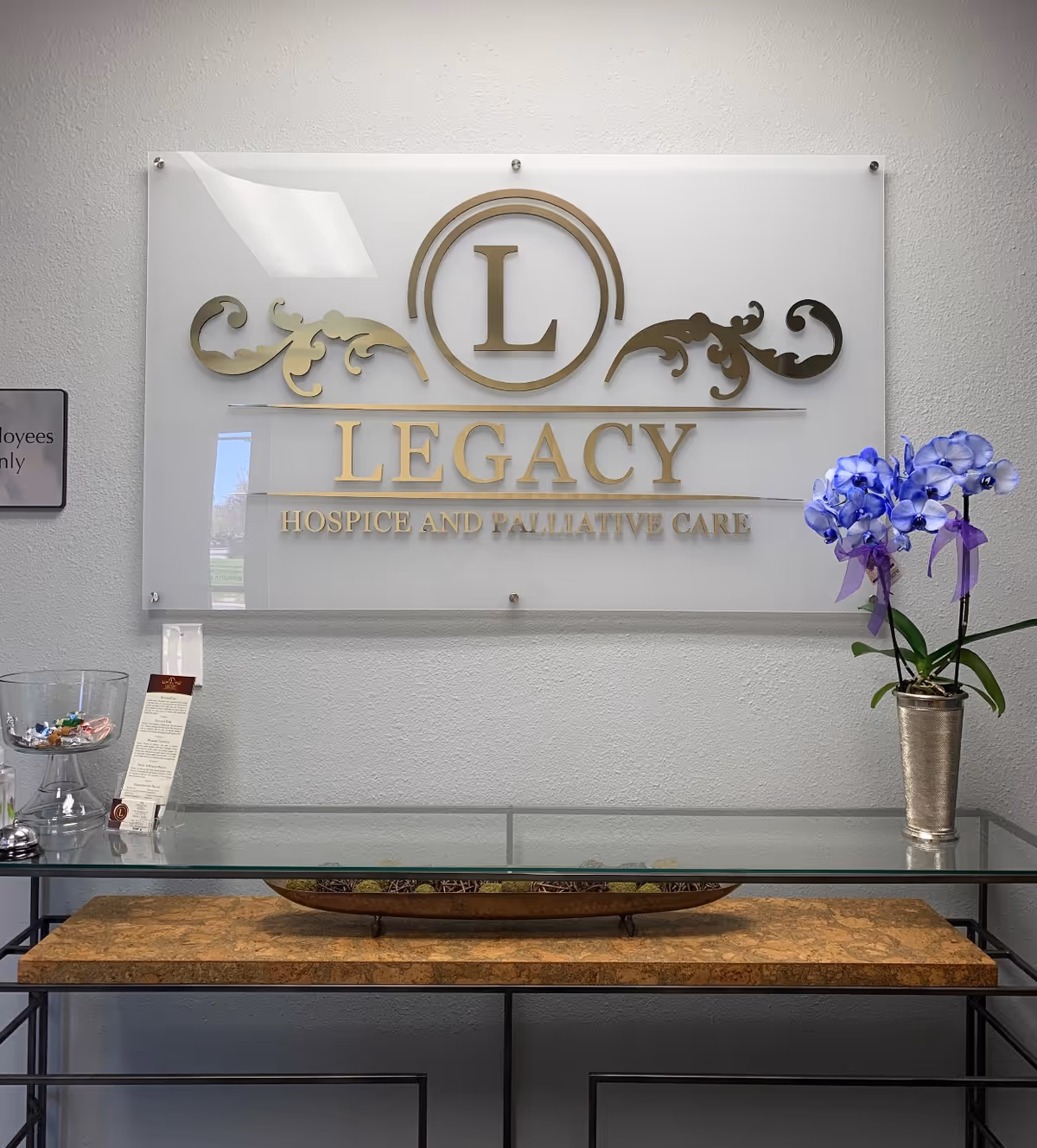 Interior lobby with a glass console, purple orchid, and Legacy Hospice and Palliative Care sign.