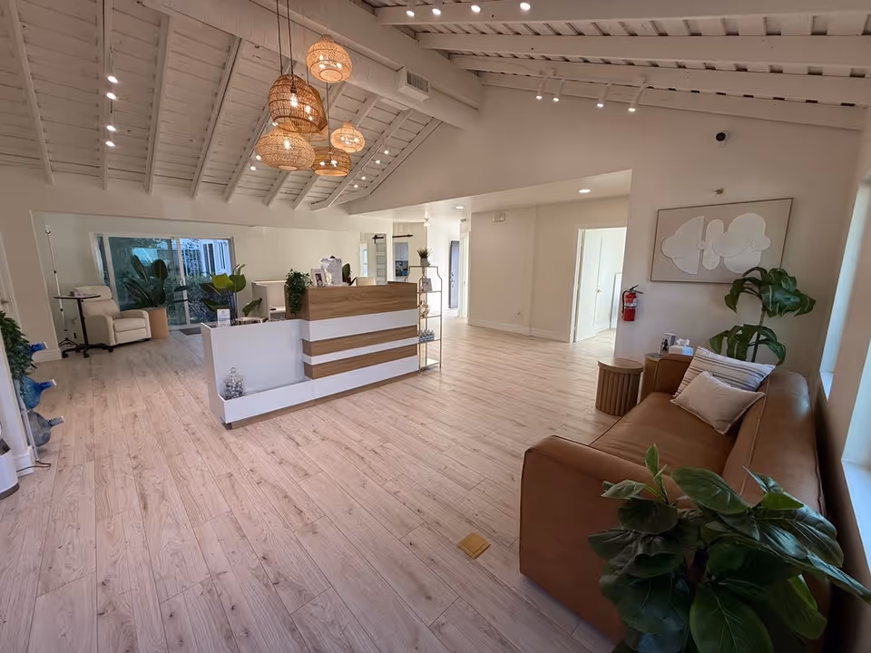 Bright reception area with a modern desk, beige sofa, pendant lights, and plants.