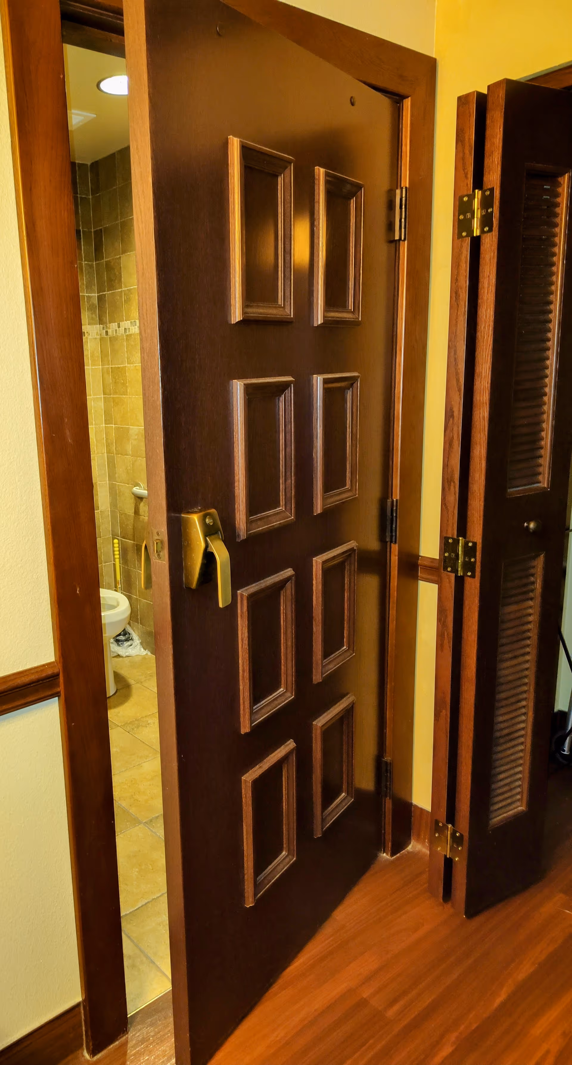 Open dark wooden door reveals a tiled bathroom with a toilet visible.
