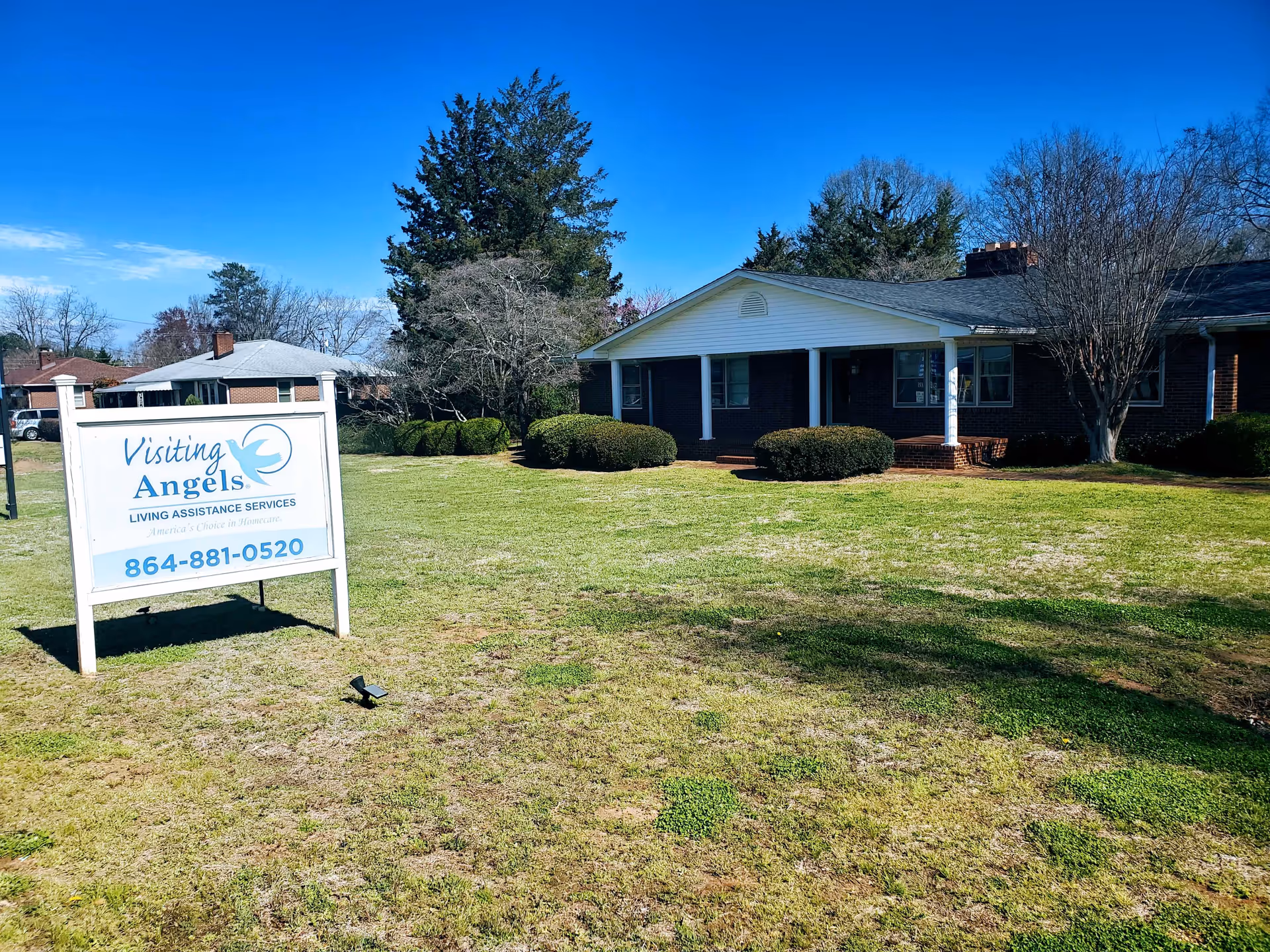 Single-story facility with a blue-brick exterior and a sign reading Visiting Angels on a grassy lawn.